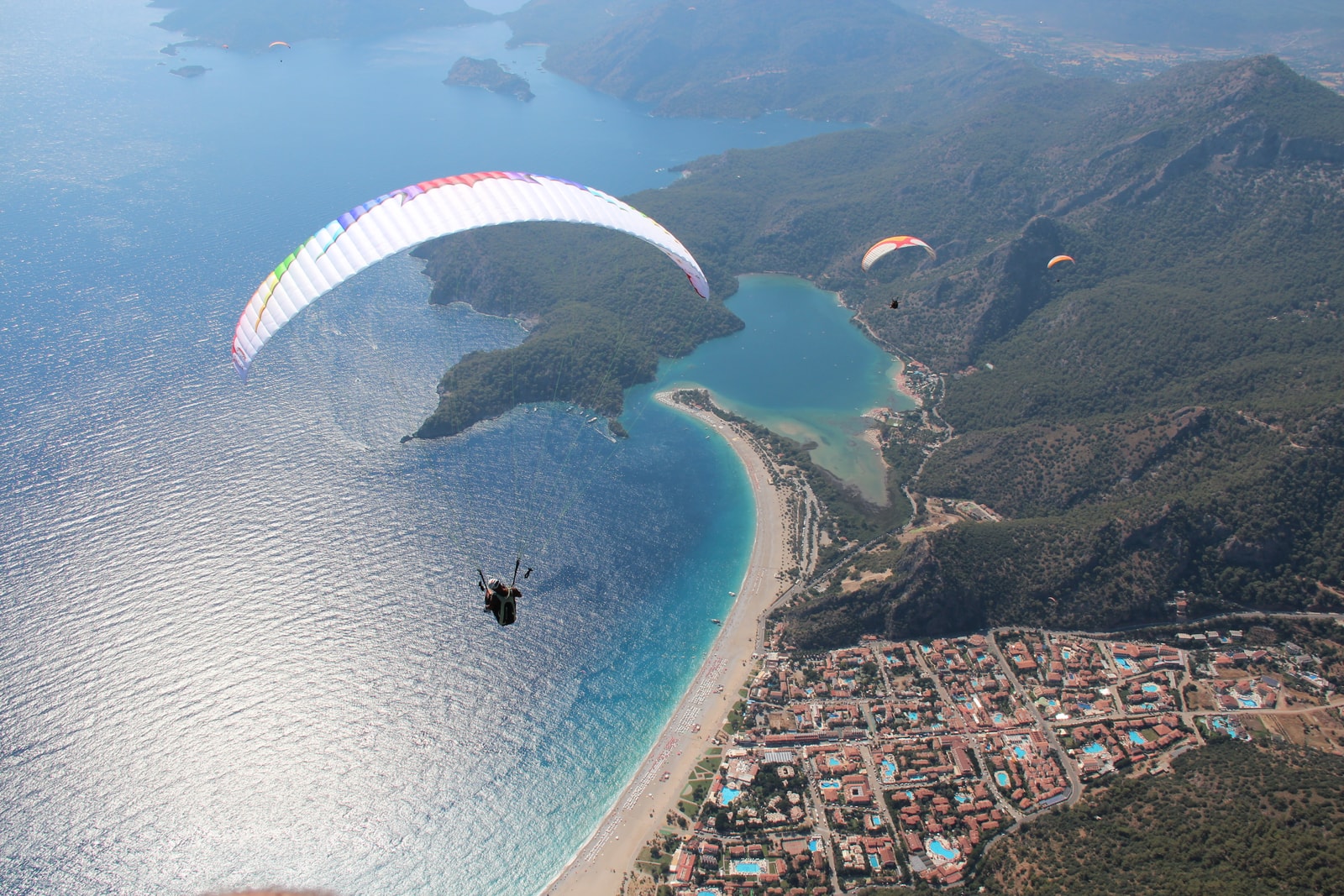 An expansive aerial view of the Ölüdeniz lagoon, beach, and resort town, with paragliders in the air.