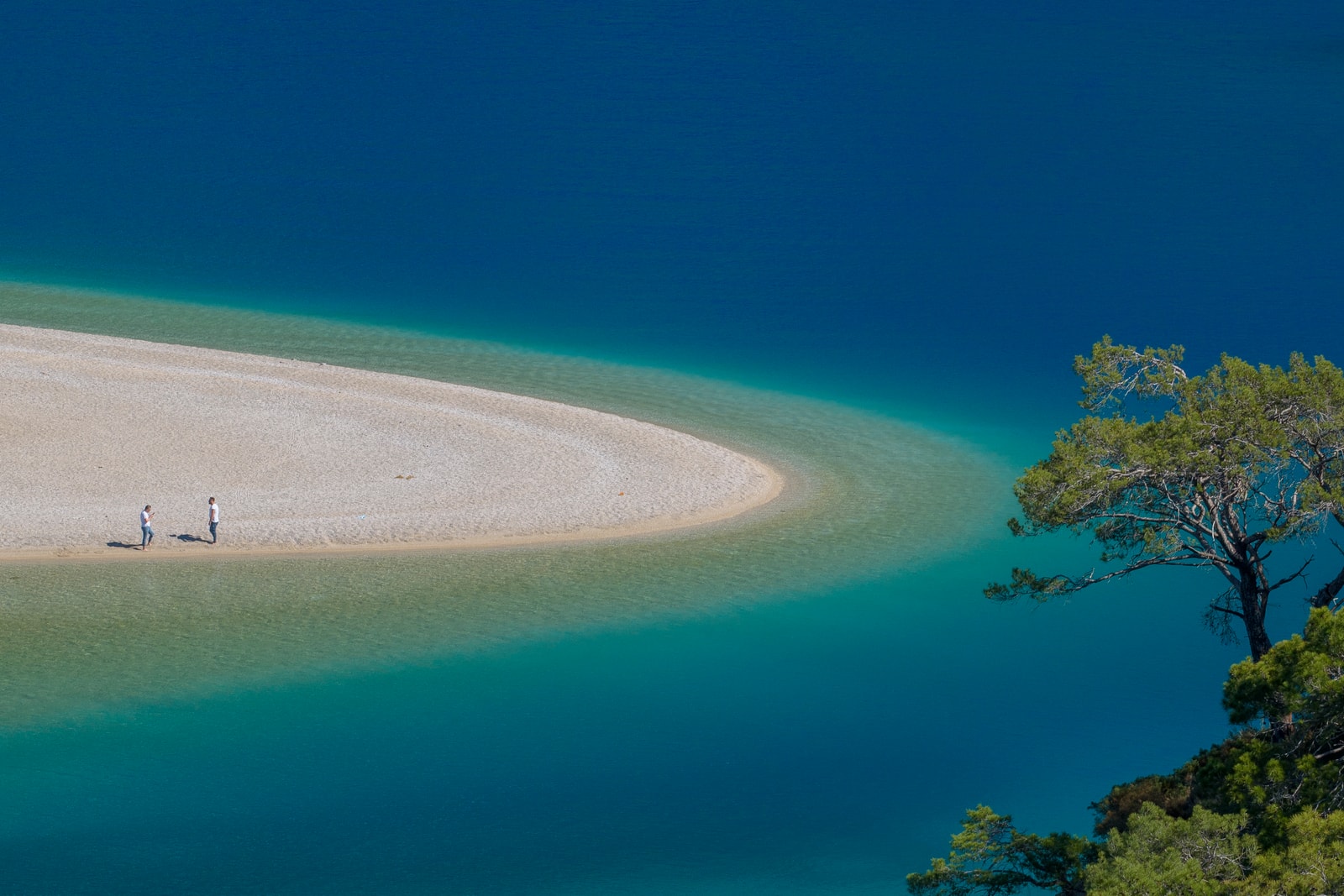 An aerial view showing a sandbar separating a calm, turquoise lagoon from the deeper blue of the open sea.