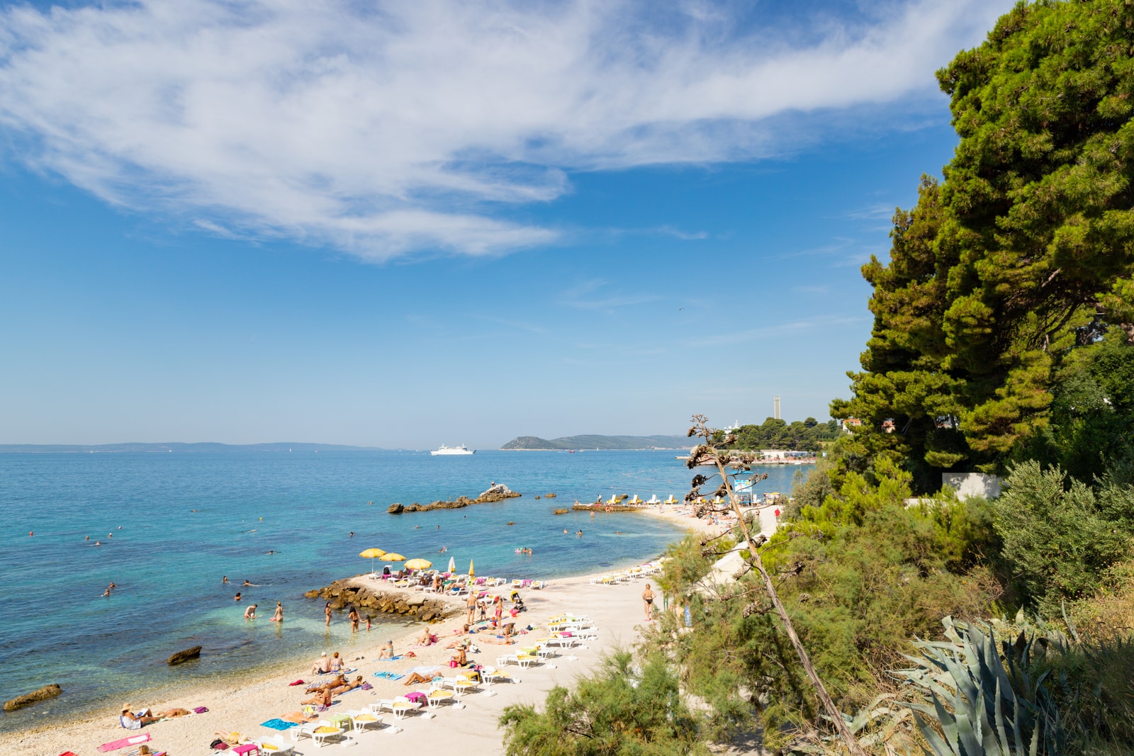 High-angle view of the cozy, rocky cove of Ovćice Beach surrounded by green pine trees and clear waters.