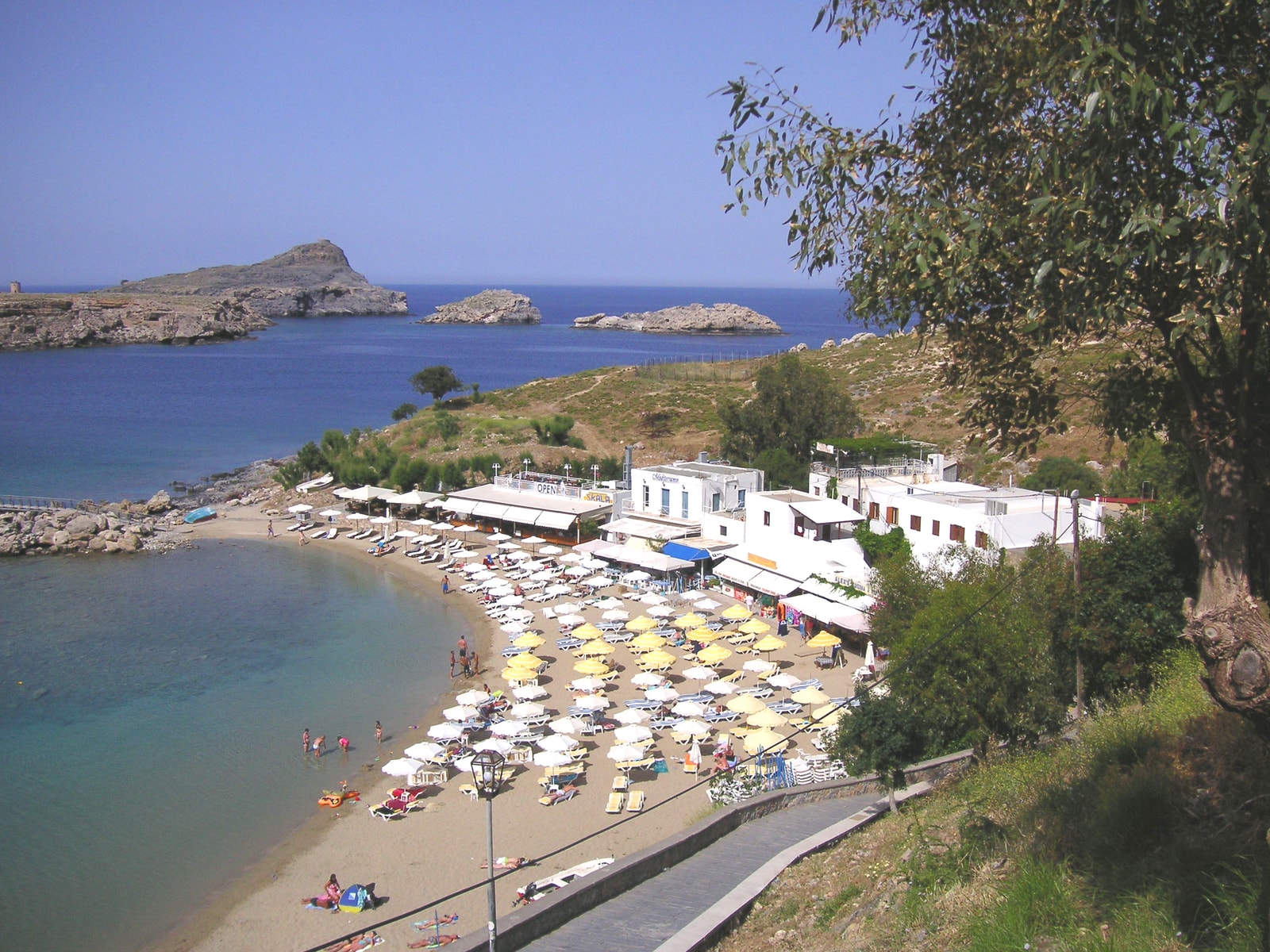 A view of the compact Pallas Beach from above, with rows of umbrellas and calm water in the bay.
