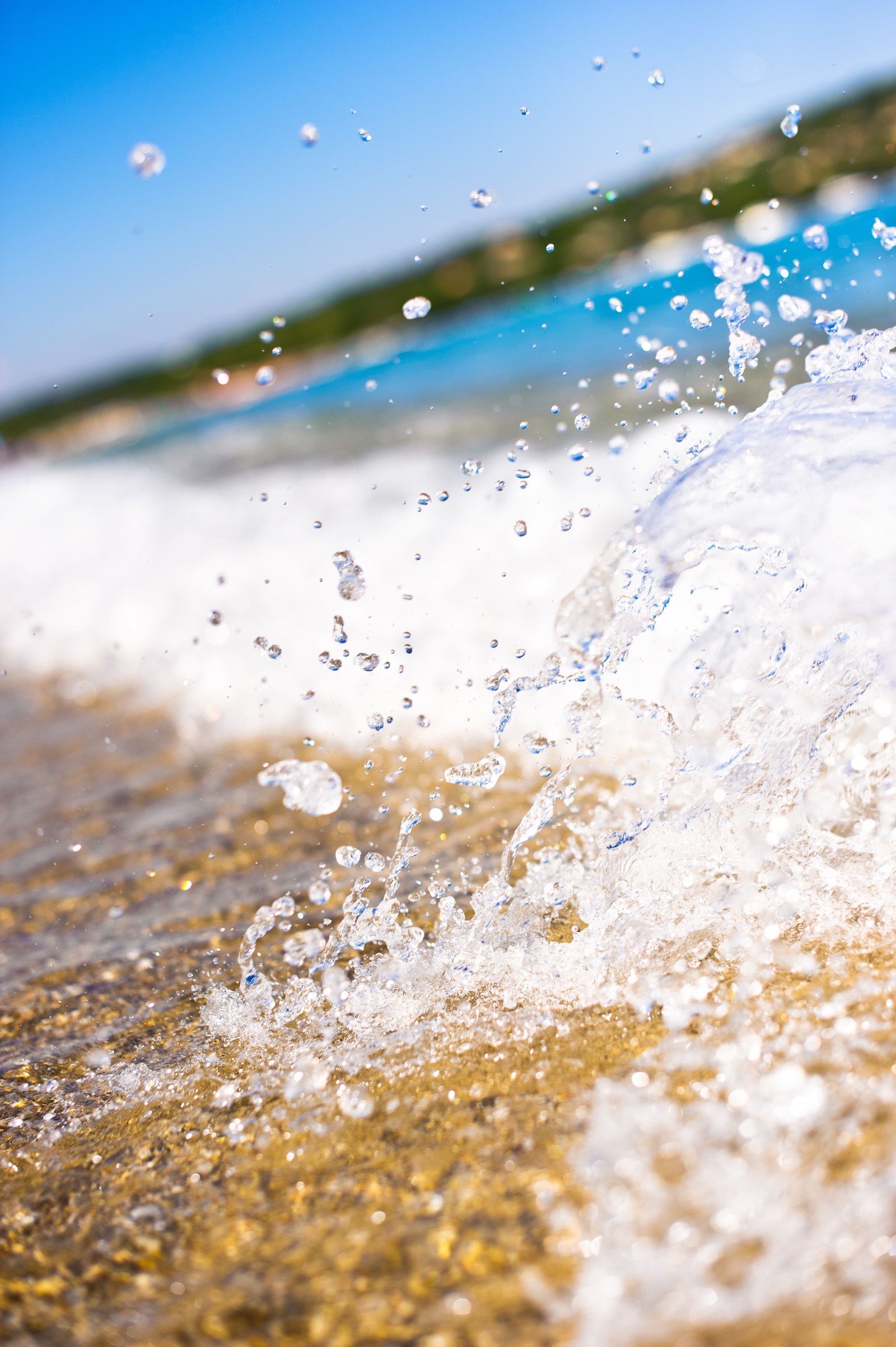 A close-up of a clear, sparkling Mediterranean wave splashing onto the golden sand of Pampelonne Beach.
