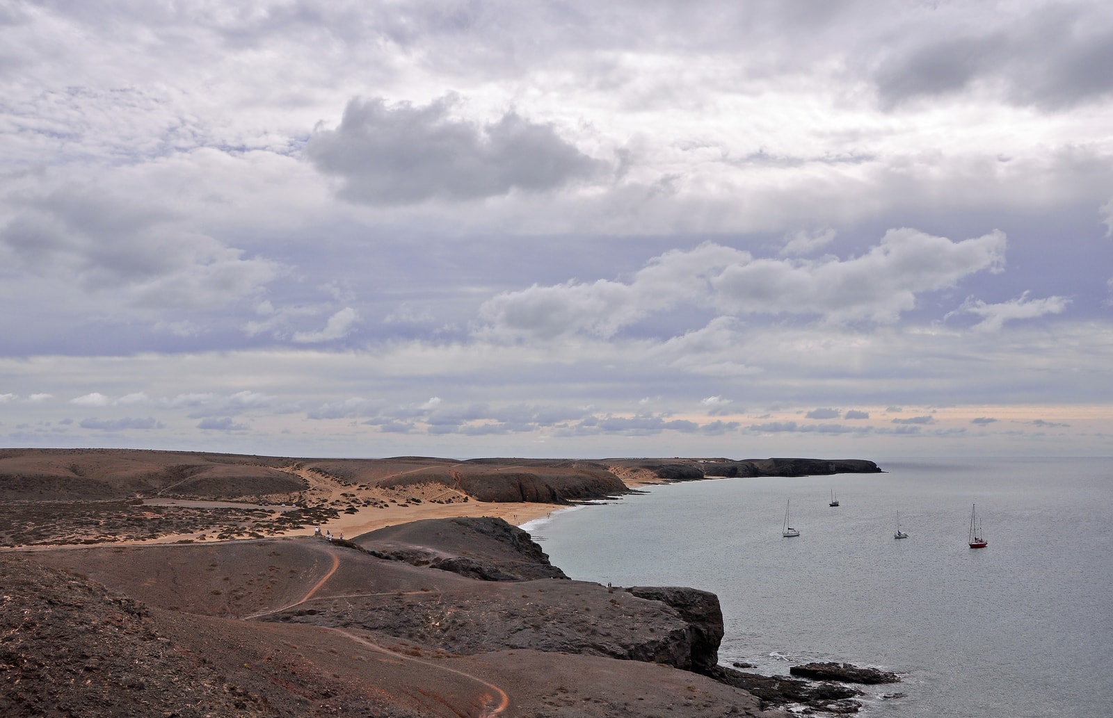 A dirt track winds through a barren, rocky landscape toward the coast.