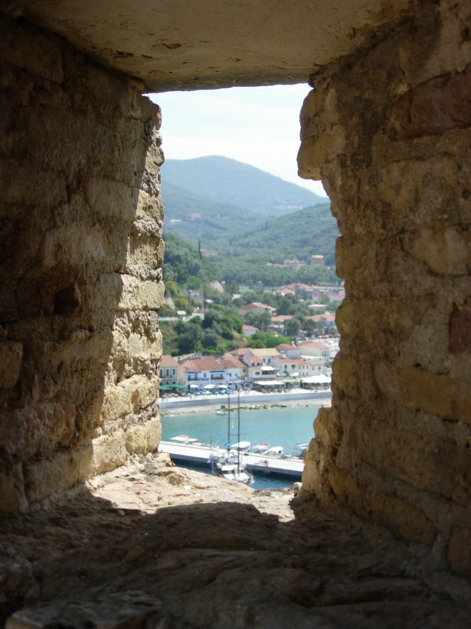 View of Parga town and harbor seen through a narrow stone loophole in the wall of the Venetian castle.