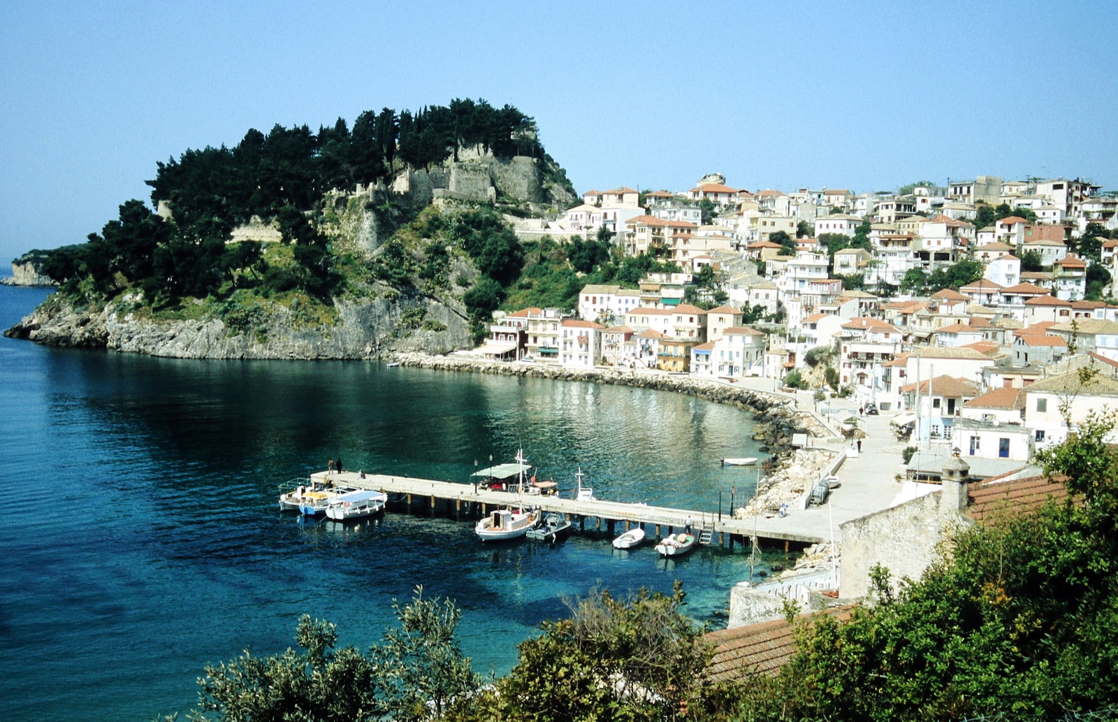 An overview of Parga town and harbor, showing the breakwater pier and buildings lining the bay.