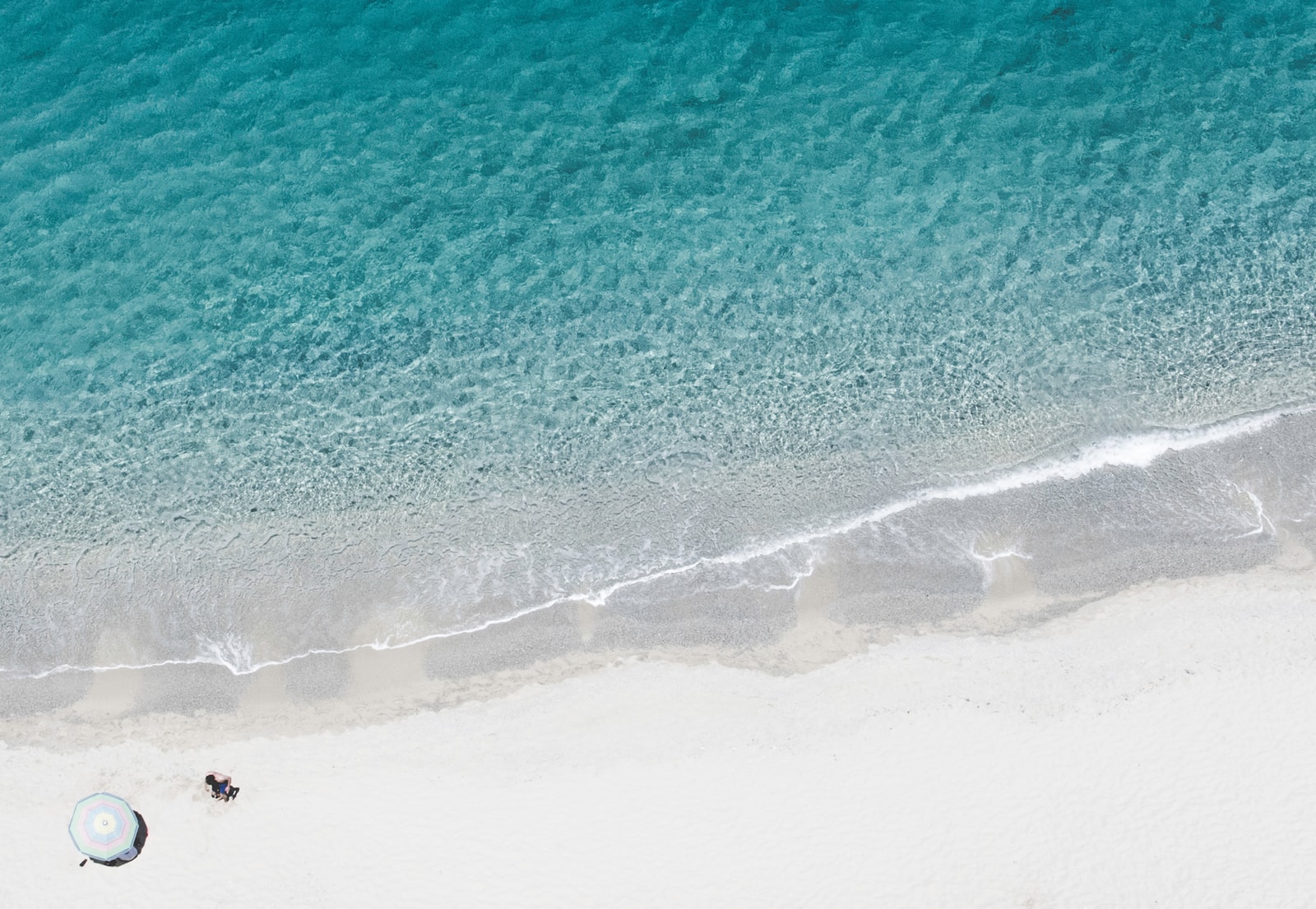 An aerial shot of a pristine beach with golden sand and dramatic granite boulders, characteristic of the wild coastline near Tropea.