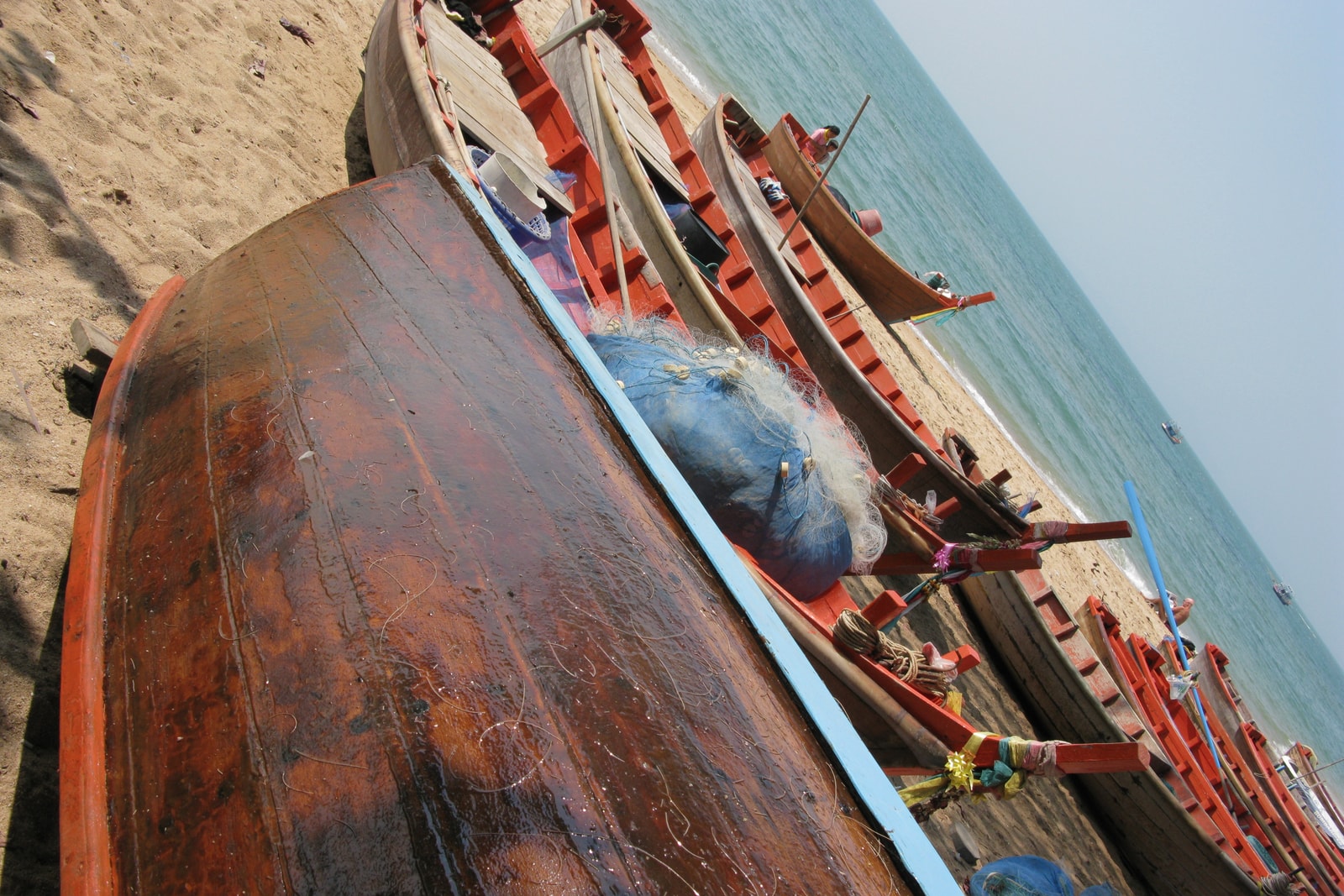 Several brightly painted wooden boats are moored on the sand at Pattaya Beach, with the city skyline in the background.
