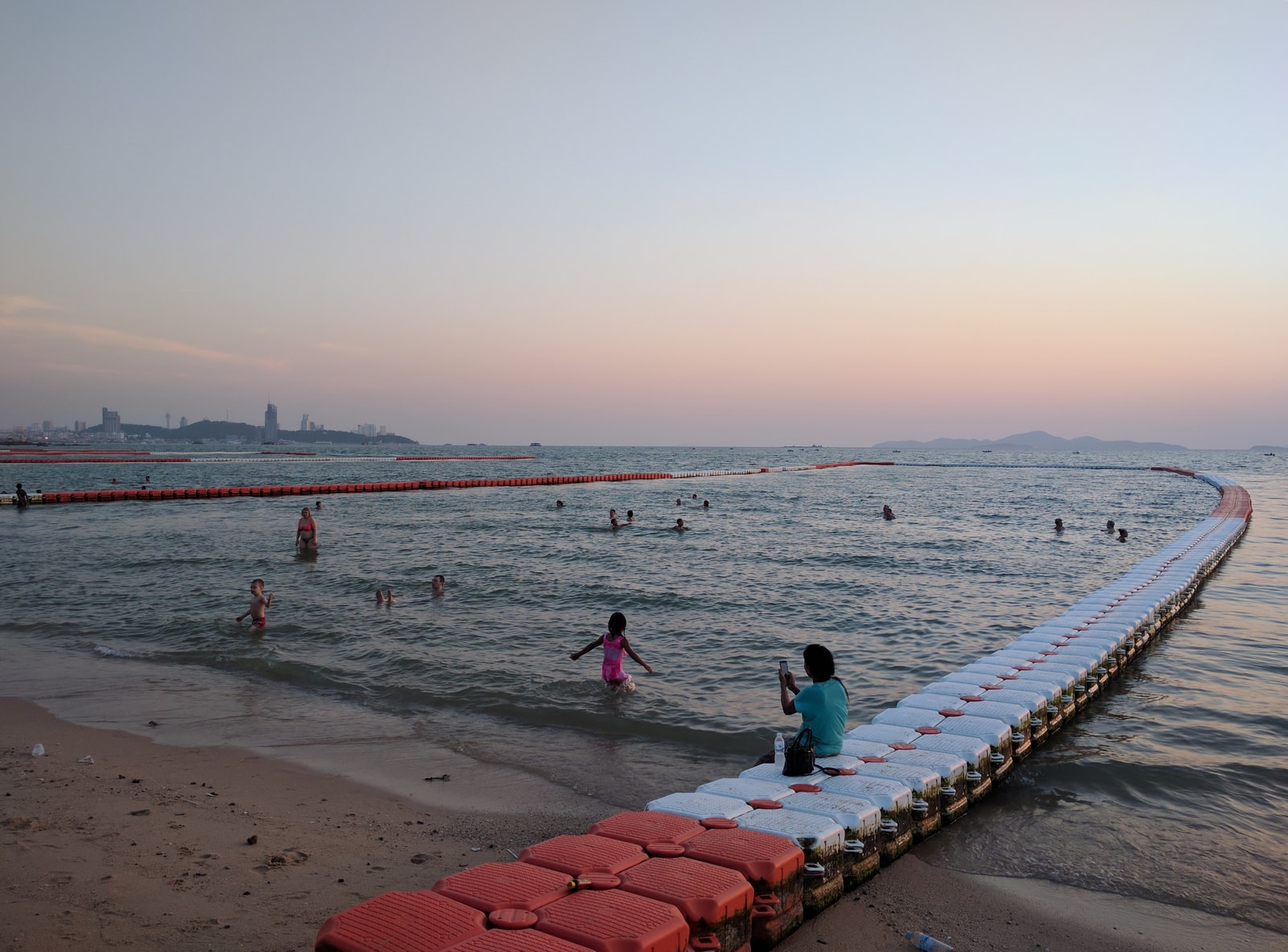 A floating yellow boom line curves through the blue-green water at Pattaya Beach, marking a designated swimming zone.