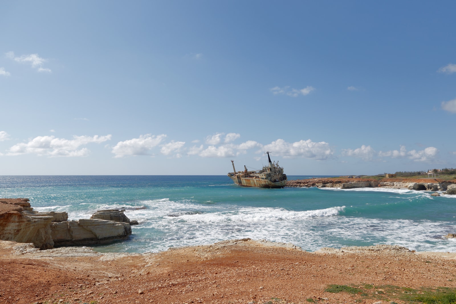 A sunny, expansive view of a rugged, rocky shoreline meeting turquoise water under a clear blue sky.