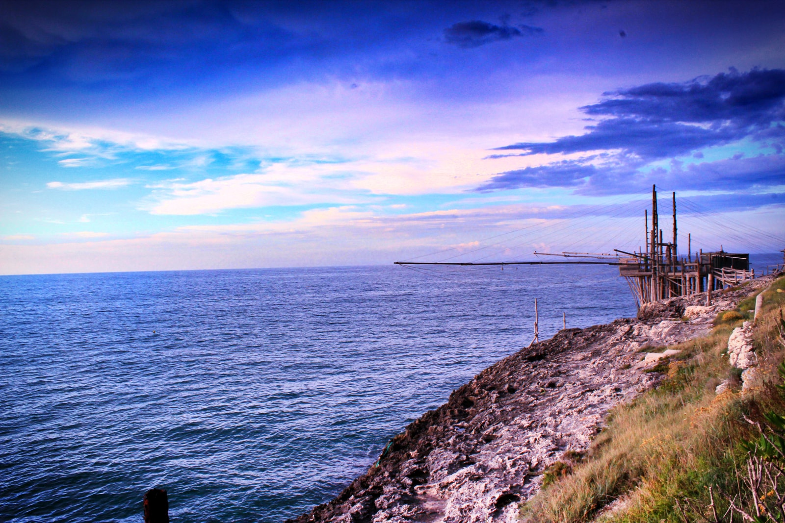 An atmospheric sunset shot of a historic wooden trabucco fishing structure on stilts, extending out over the Adriatic Sea in Peschici.