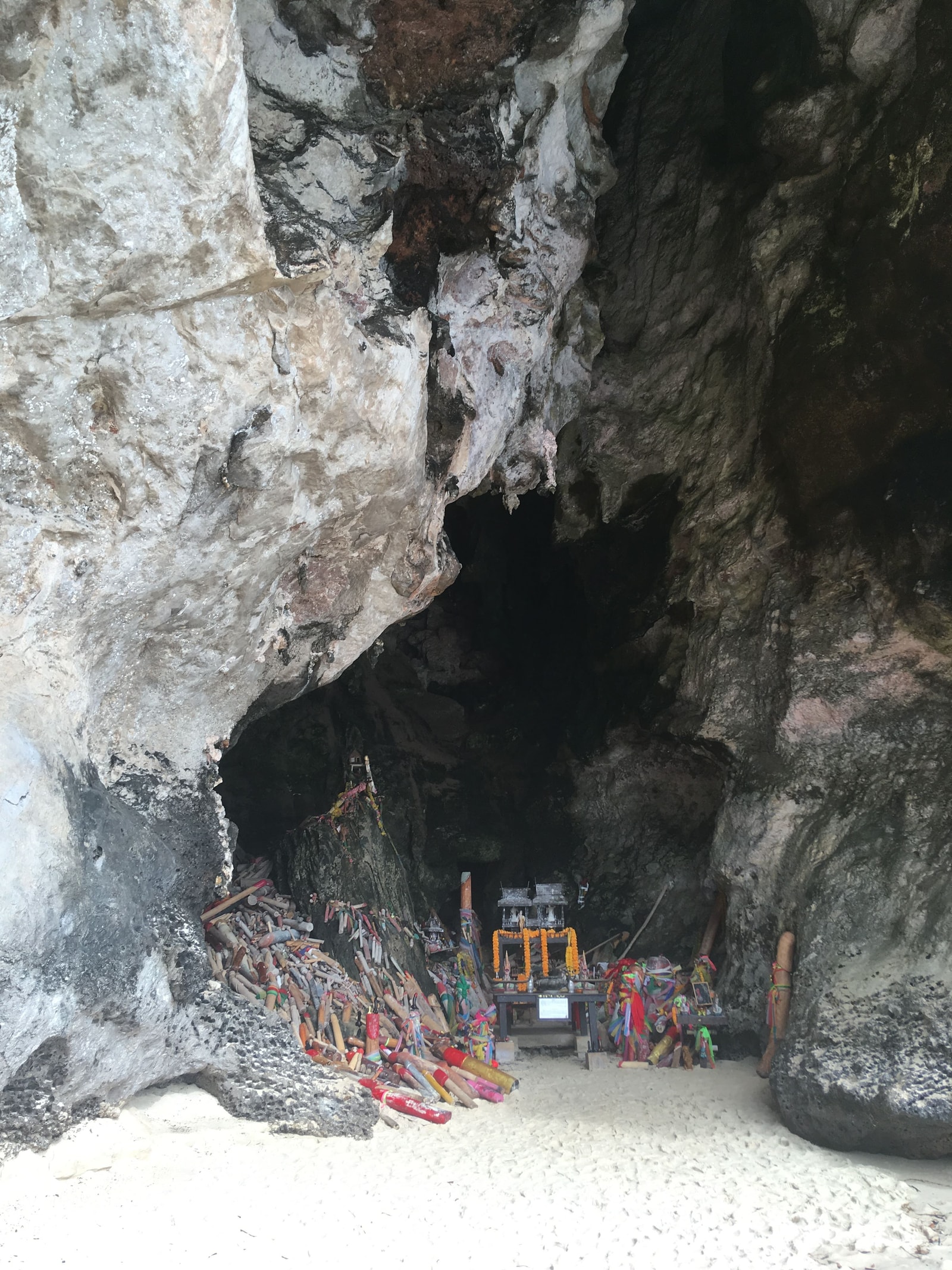 A view from inside a cave looks out onto a sunny beach, with numerous symbolic offerings placed on a shrine in the foreground.