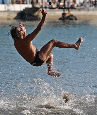 A close-up action photograph of an athletic Picigin player making a spectacular backward dive in Split.