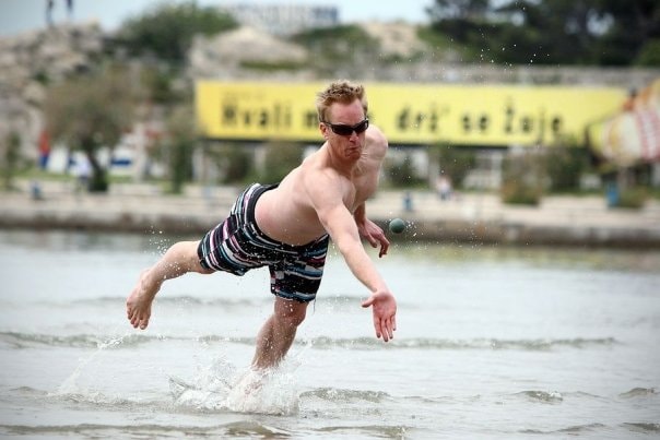 Action shot capturing a player running and lunging forward through shallow sea water to strike the ball.