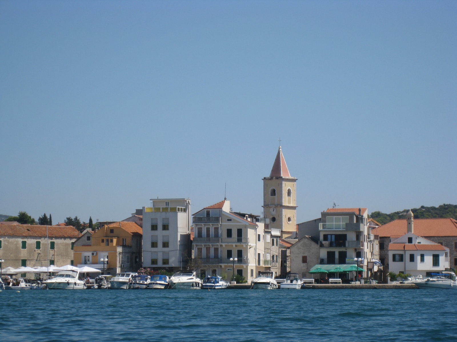 A view of the Pirovac waterfront from the sea, showing the town's traditional buildings and the central church bell tower.