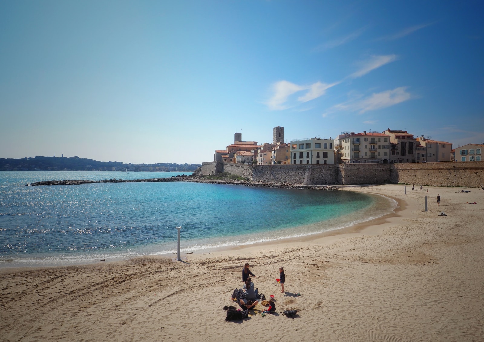 A panoramic view of Plage de la Gravette shows the calm, shallow water and the historic fortified town walls rising from the sea.