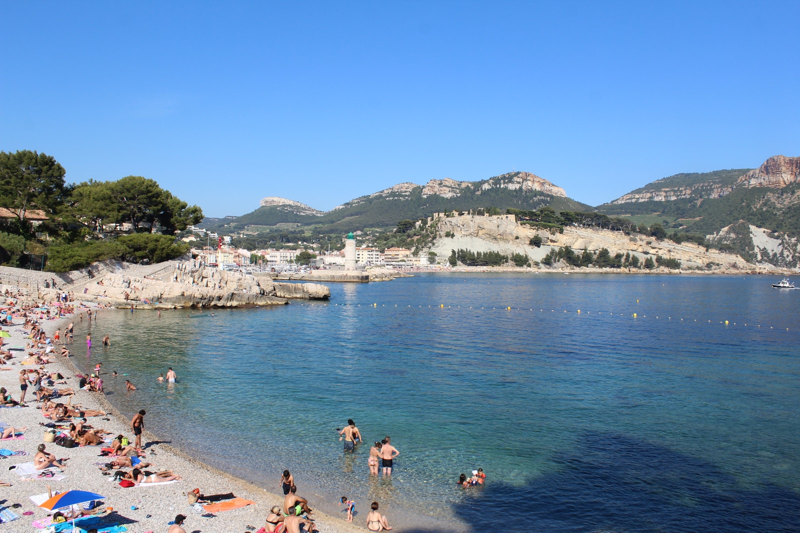 A scenic view of Plage de la Grande Mer with the historic Cassis Castle standing on the cliffs overlooking the beach and the blue water of the cove.