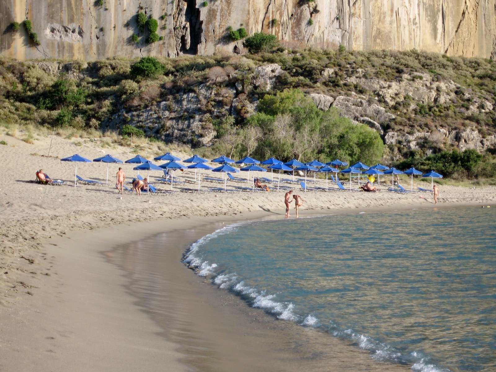 Swimmers and sunbathers enjoy the sandy cove of Plakias under a high pale cliff