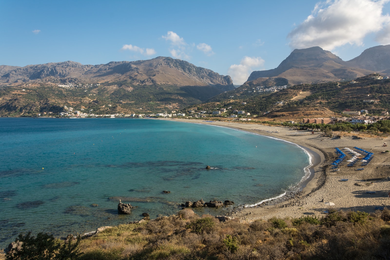 A curving shoreline leads towards a settlement backed by a rugged mountain ridge