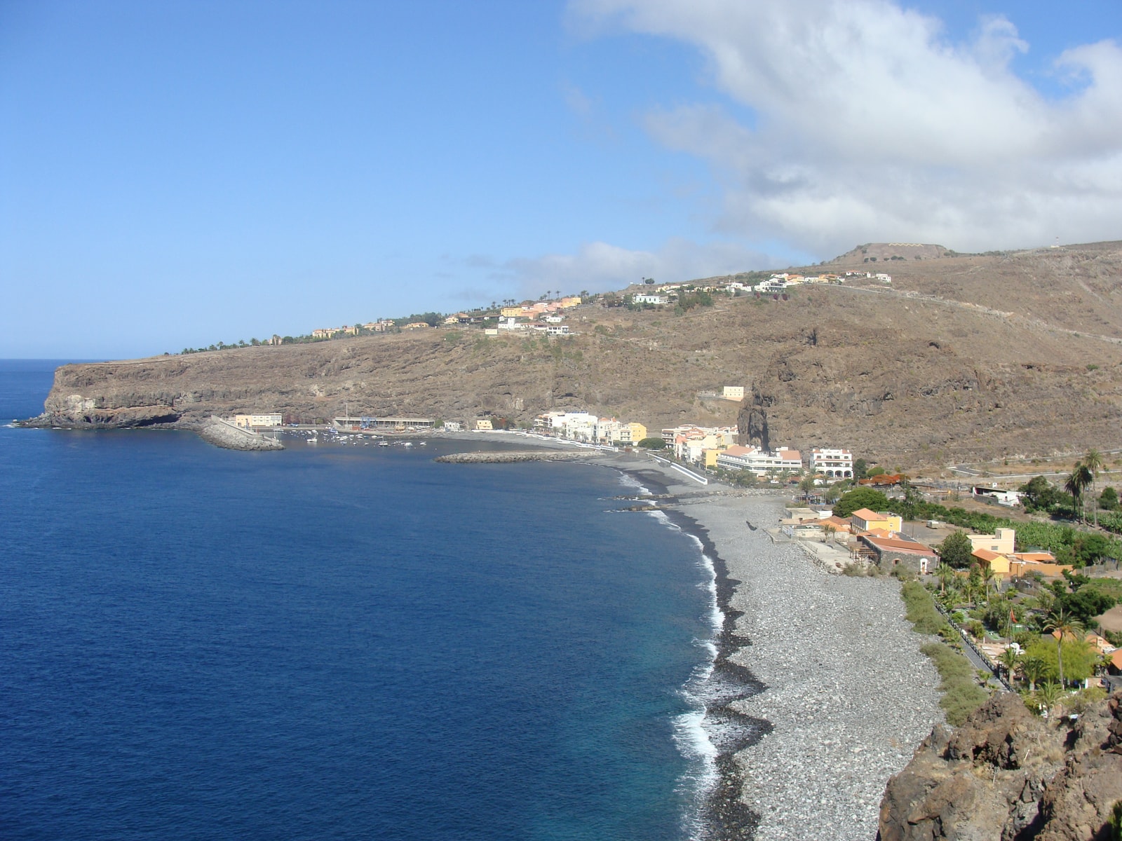 An aerial overview of Playa de Santiago, showing the dark shoreline, the town, the bay, and the surrounding dry volcanic landscape.