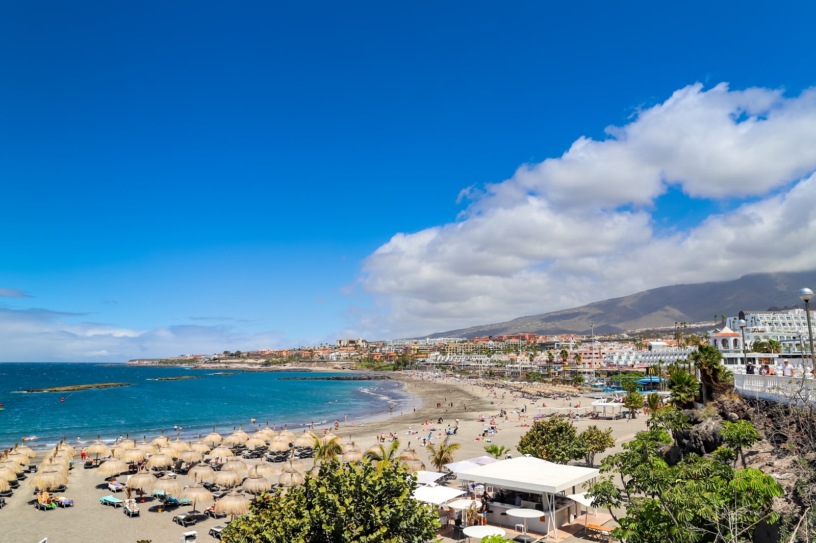 An aerial view of Playa de Torviscas, showing a sheltered bay with many sun loungers and umbrellas on the sand.
