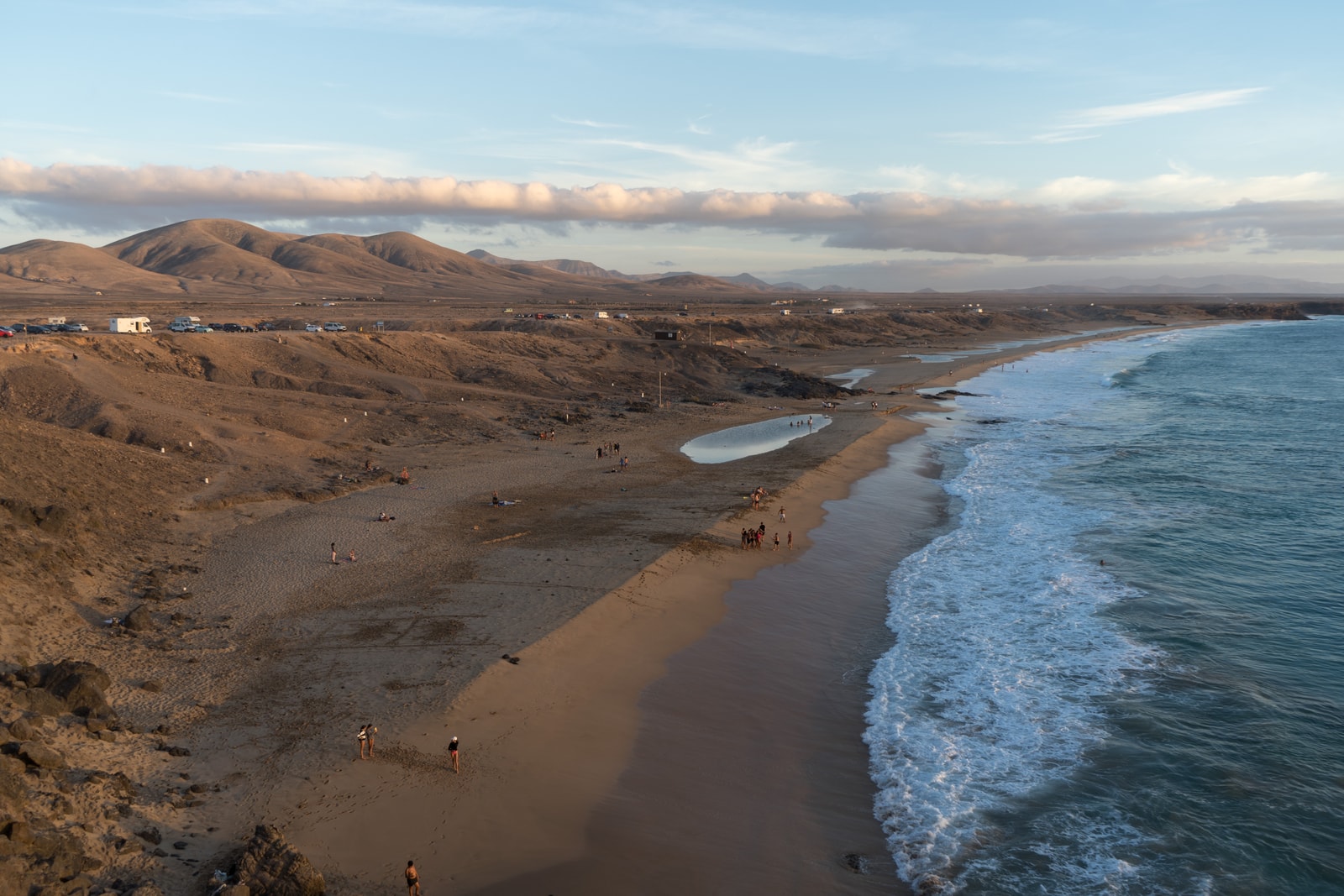 An overhead view of Playa del Castillo, showing a wide expanse of golden sand, powerful surf, and dark cliffs.