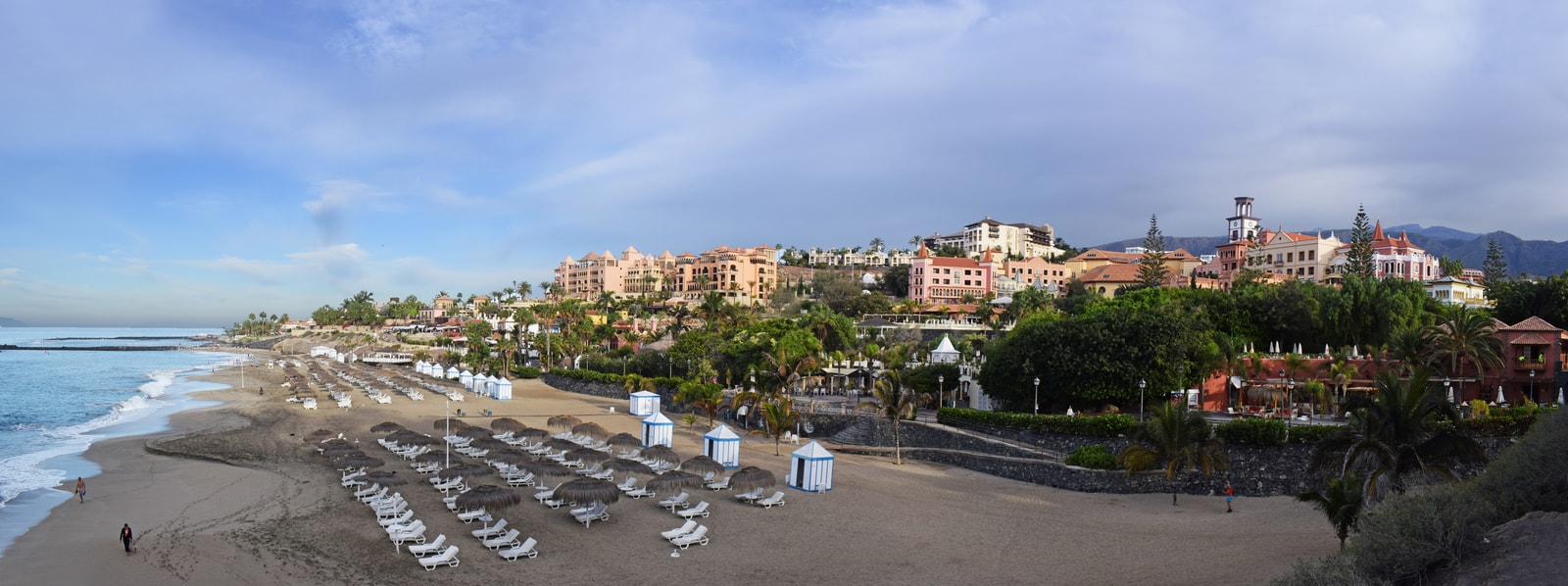 A panoramic view of Playa Del Duque, showing its golden sand, turquoise water, and thatched umbrellas.