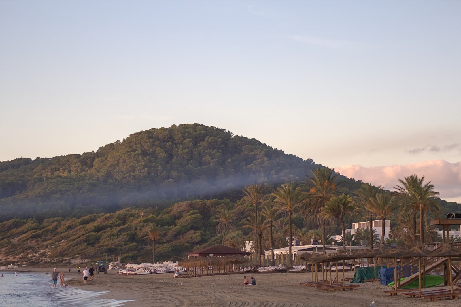 A serene view of Playa d'en Bossa at dawn, with thatched parasols on the sand and calm waters.