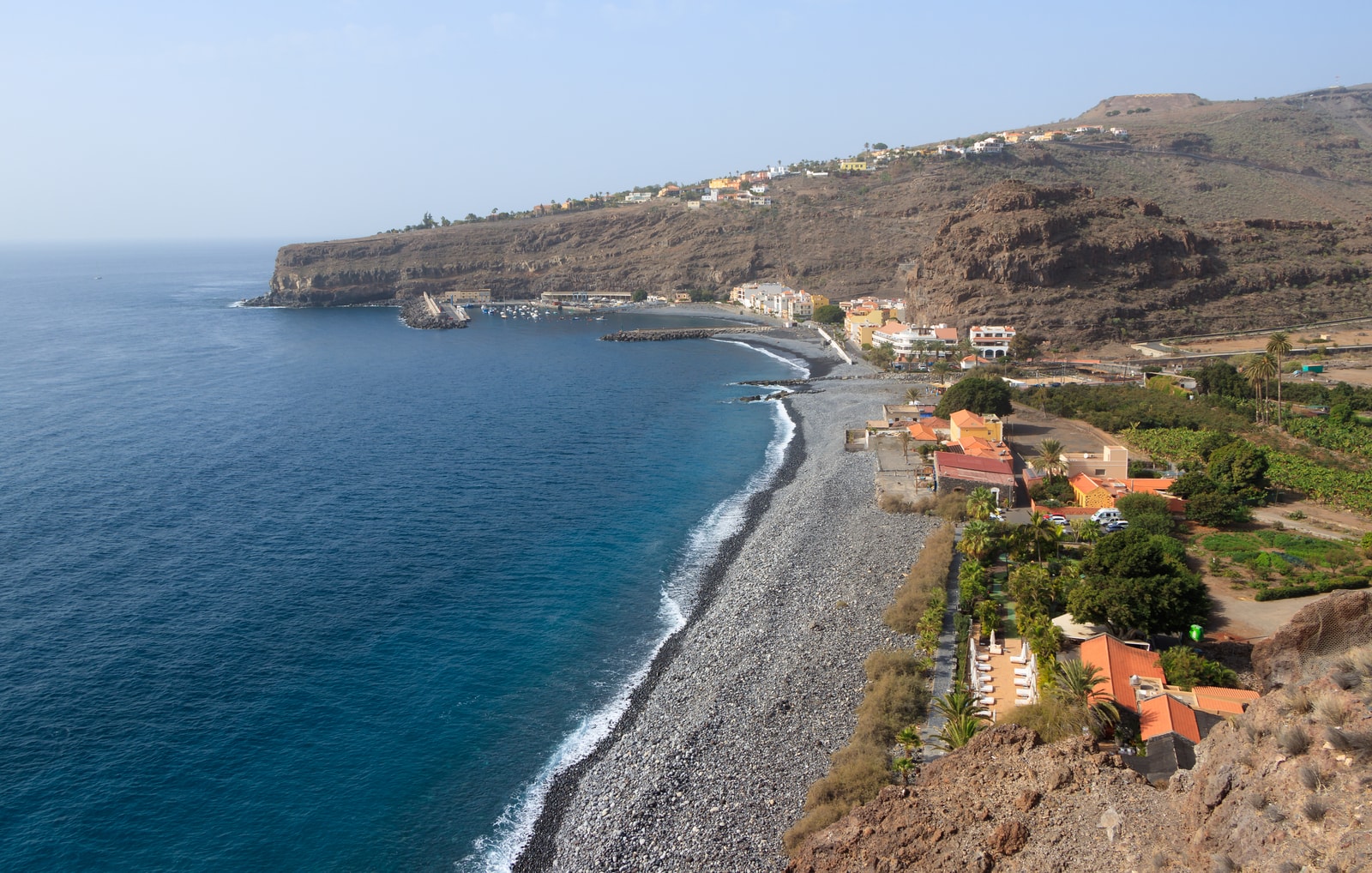 A view of Playa Santiago's coastline from the sea, showing the harbor, town, and volcanic headlands under a clear sky.