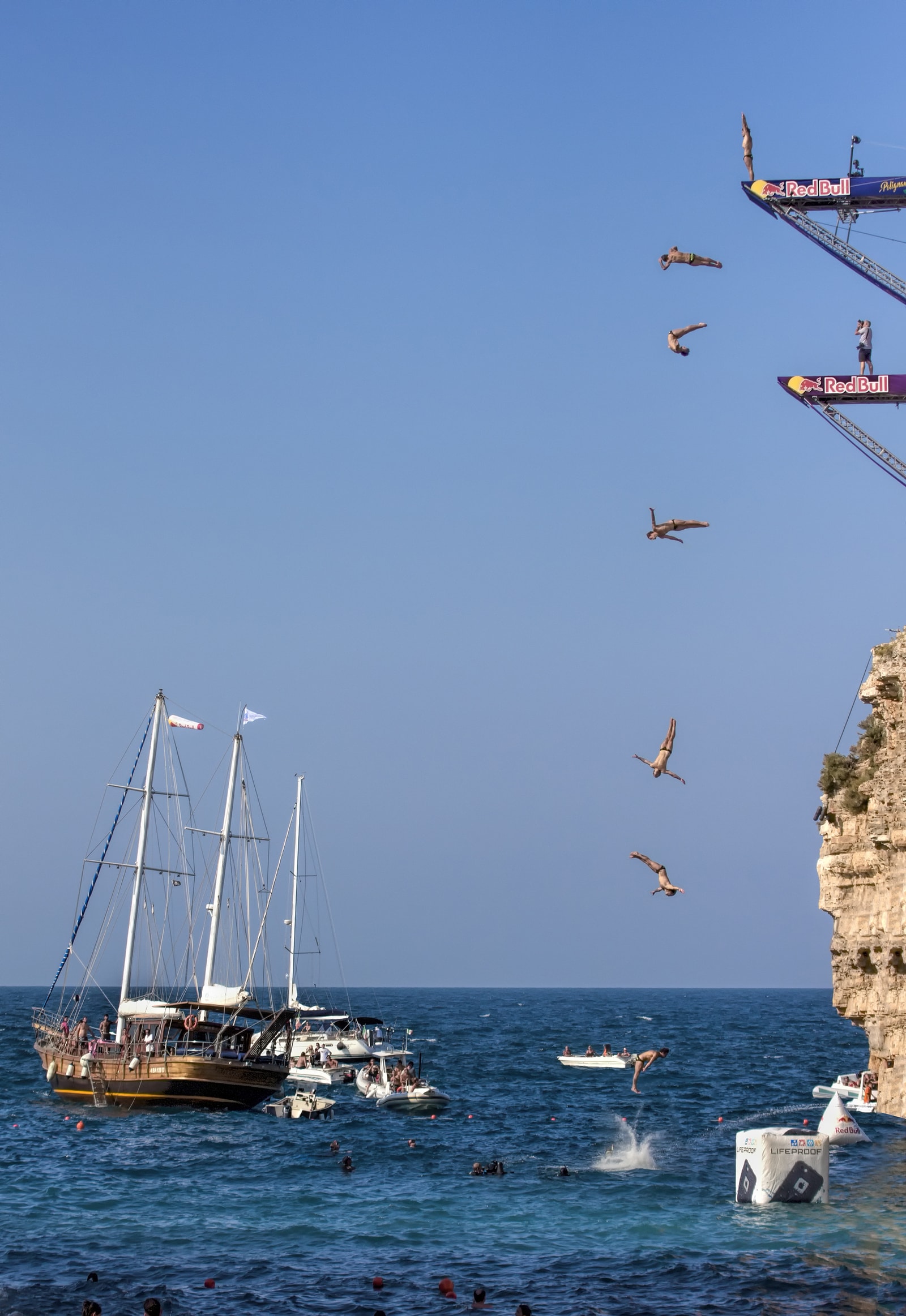 A professional diver in mid-air, having launched from a high platform mounted on the cliffs of Polignano a Mare during the Red Bull Cliff Diving event.