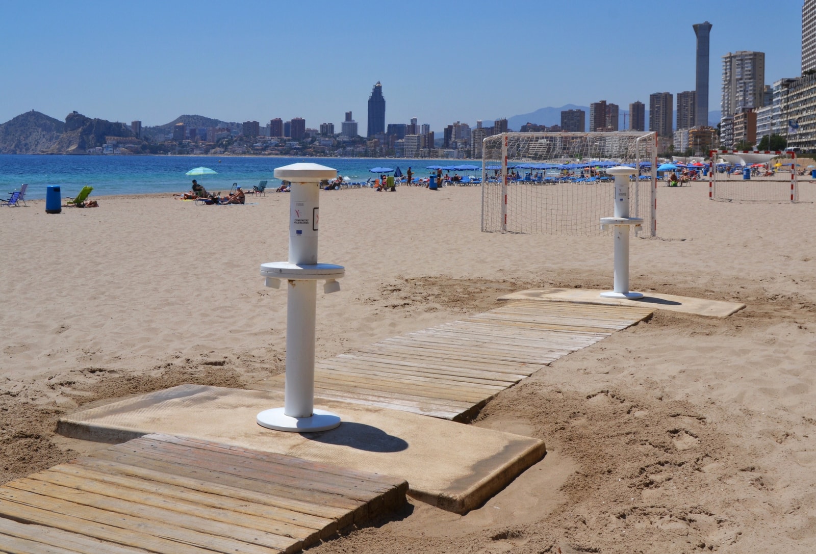 Modern footwashers on Poniente Beach with wooden boardwalks and a sand volleyball court.