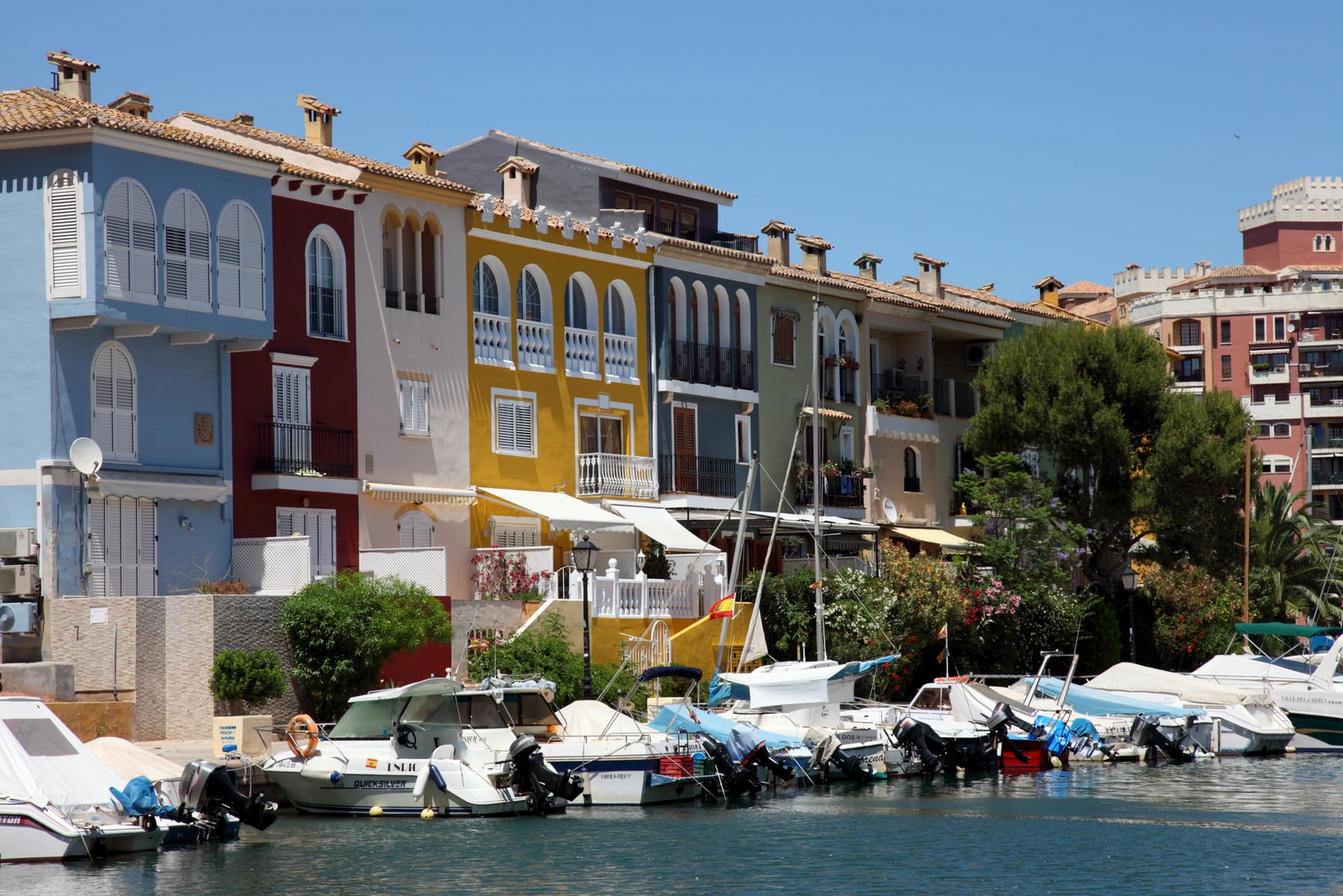 Pastel-colored Mediterranean townhouses in terracotta, ochre, and blue lining a tranquil canal in Port Saplaya.