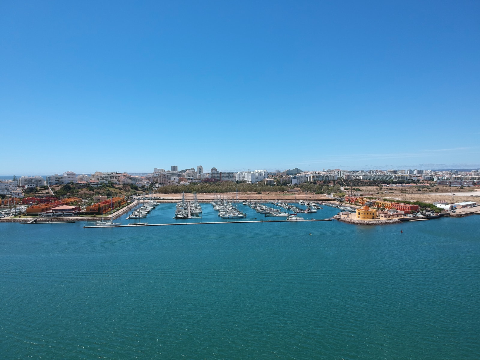 An aerial view of Portimão Marina, showing docks filled with boats, waterfront buildings, and the surrounding city.