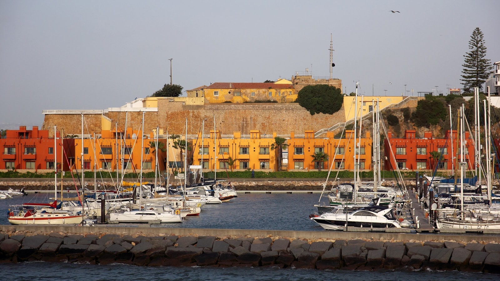 Sailboats moored in Portimão Marina, with the Fortaleza de Santa Catarina visible across the water.