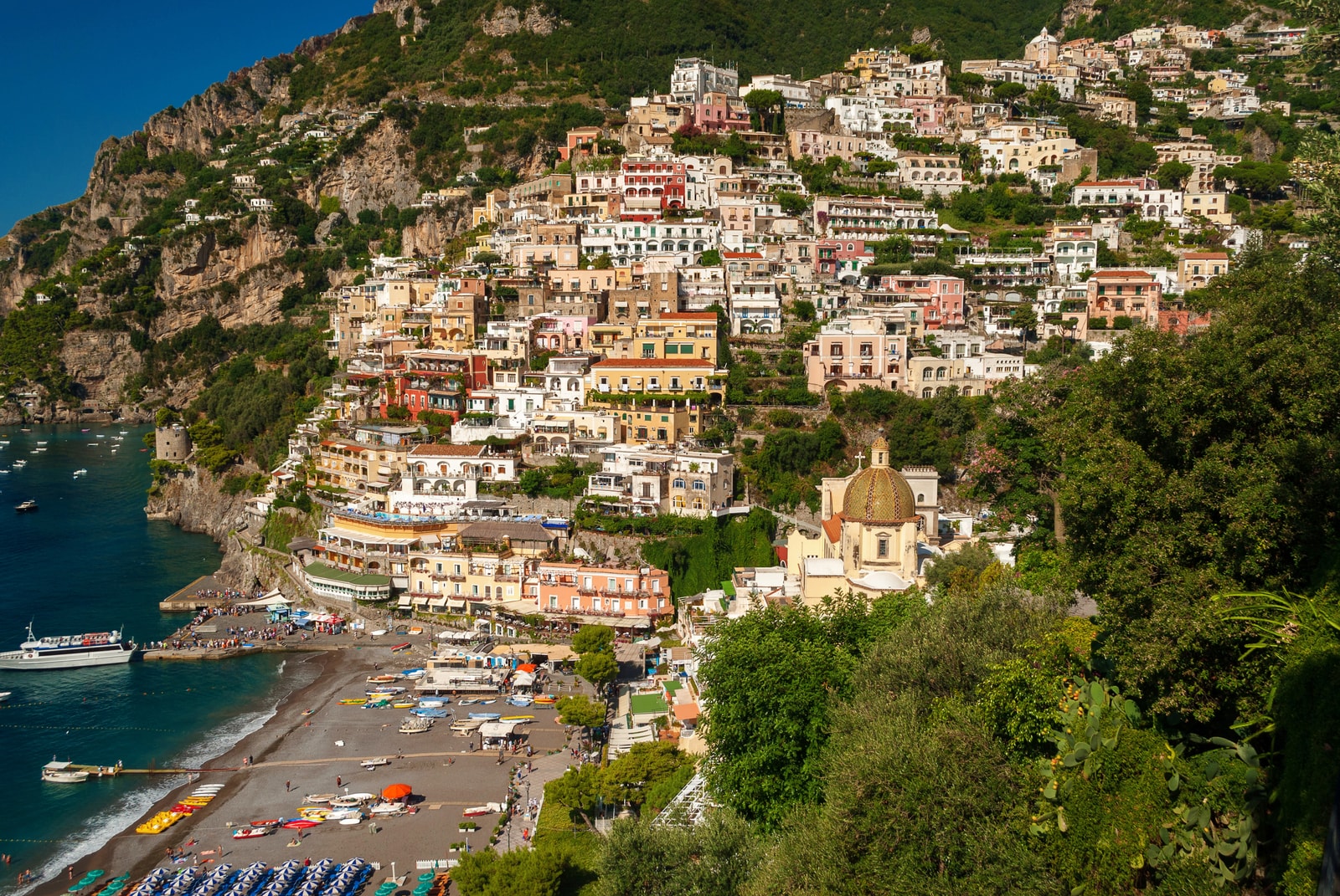 A panoramic view shows Positano's beach, domed church, and mountainside buildings.