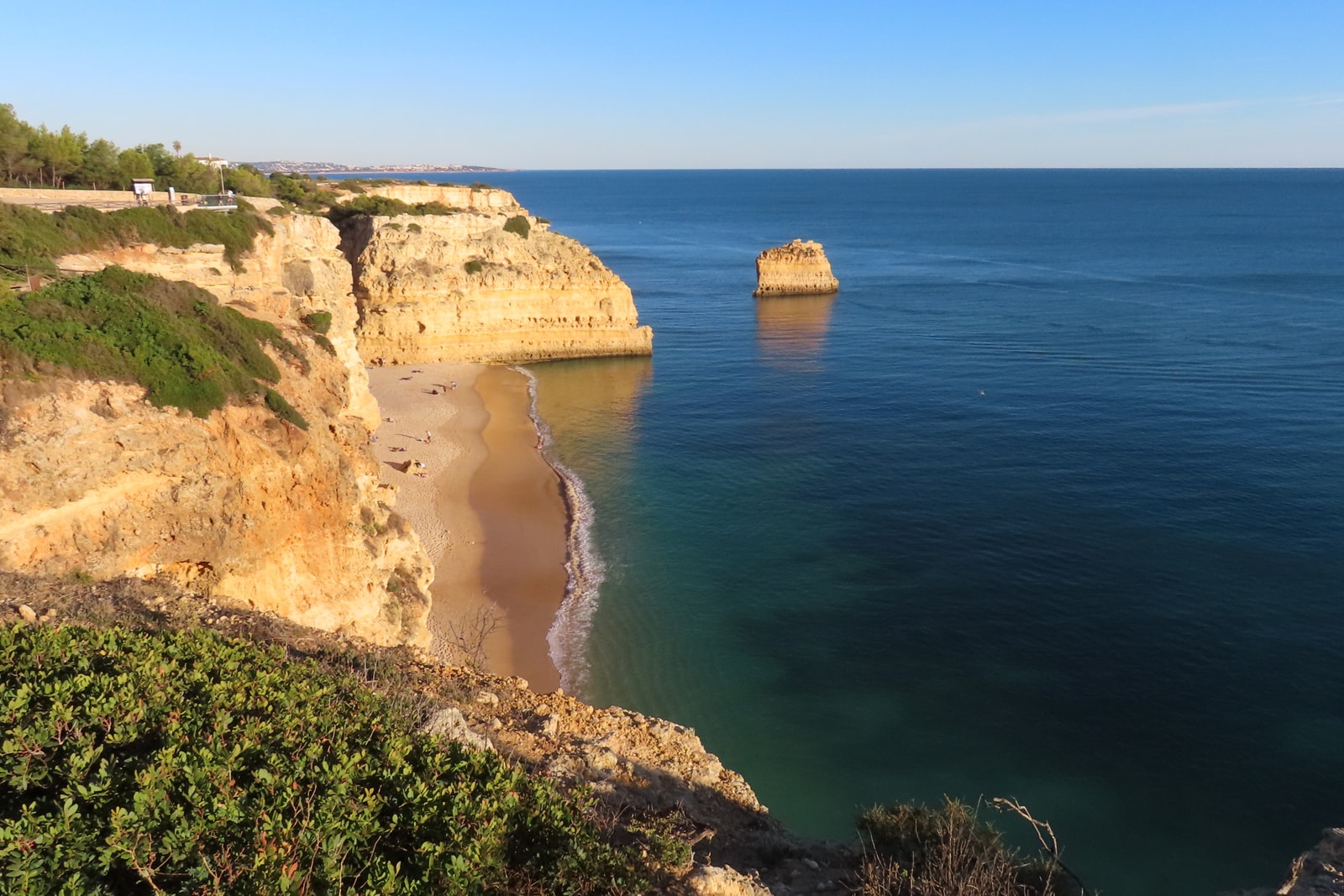 An elevated view of a sandy cove with turquoise water, surrounded by golden cliffs and a prominent sea stack.
