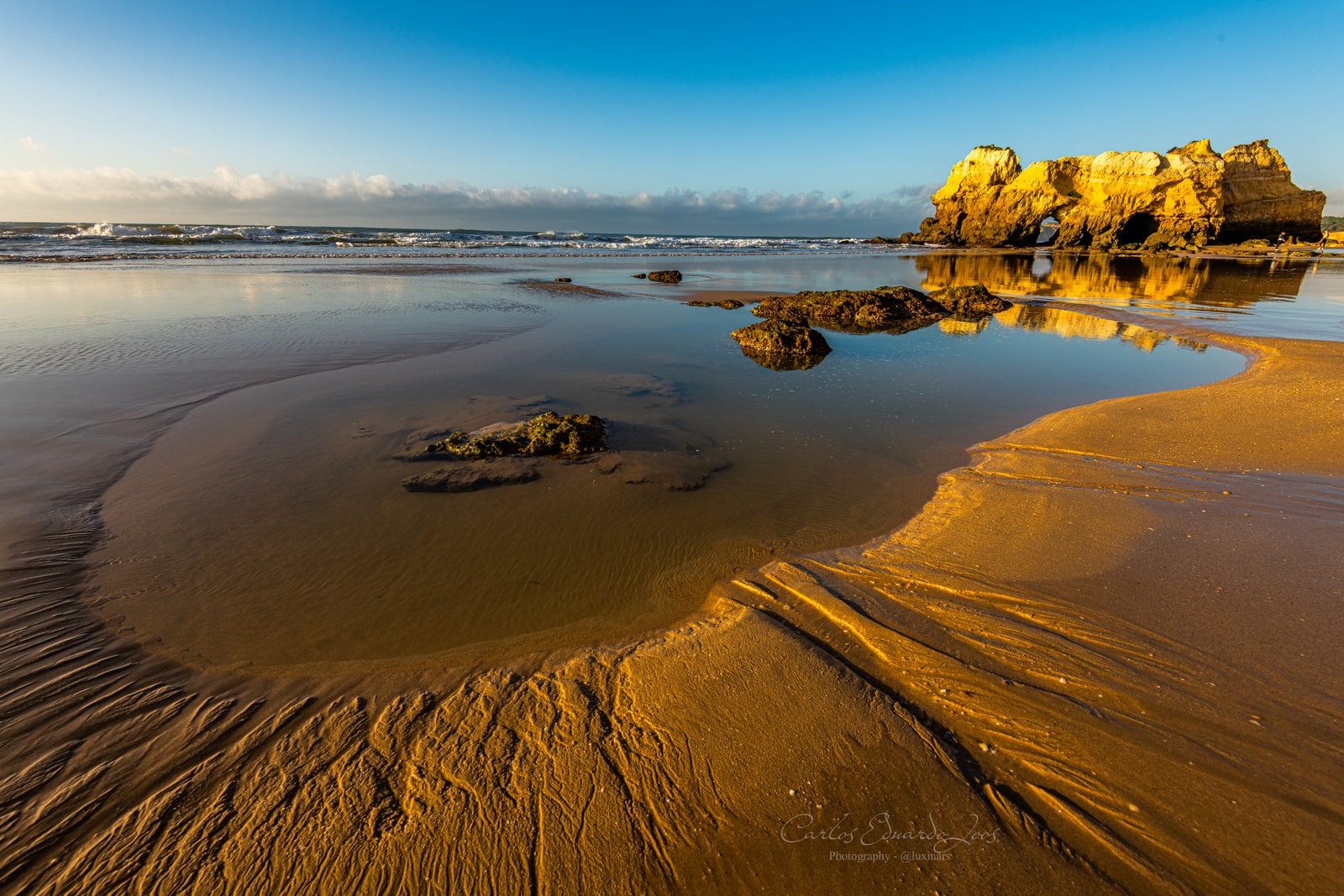 The wet sand at Praia da Rocha reflects the golden light of sunset, with rugged rock formations silhouetted against the sky.
