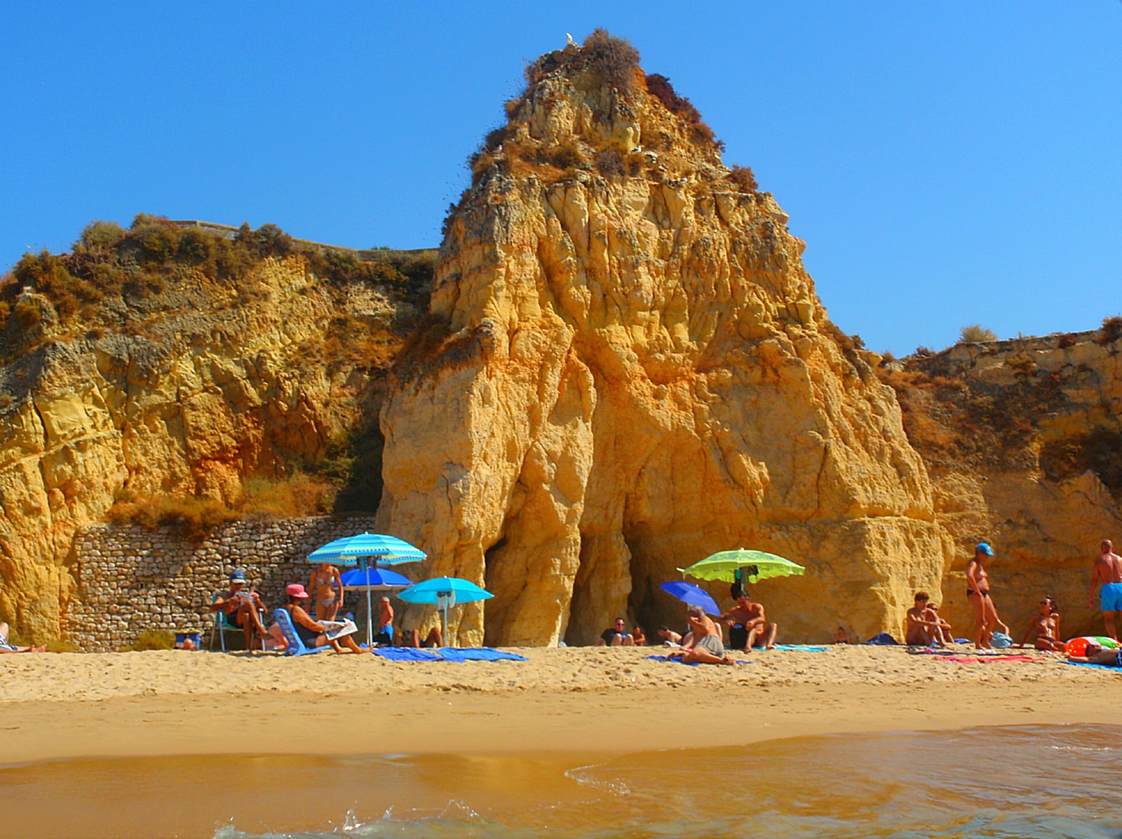 A close-up view of an ochre-colored rock formation rising from the sandy cove at Praia da Rocha.