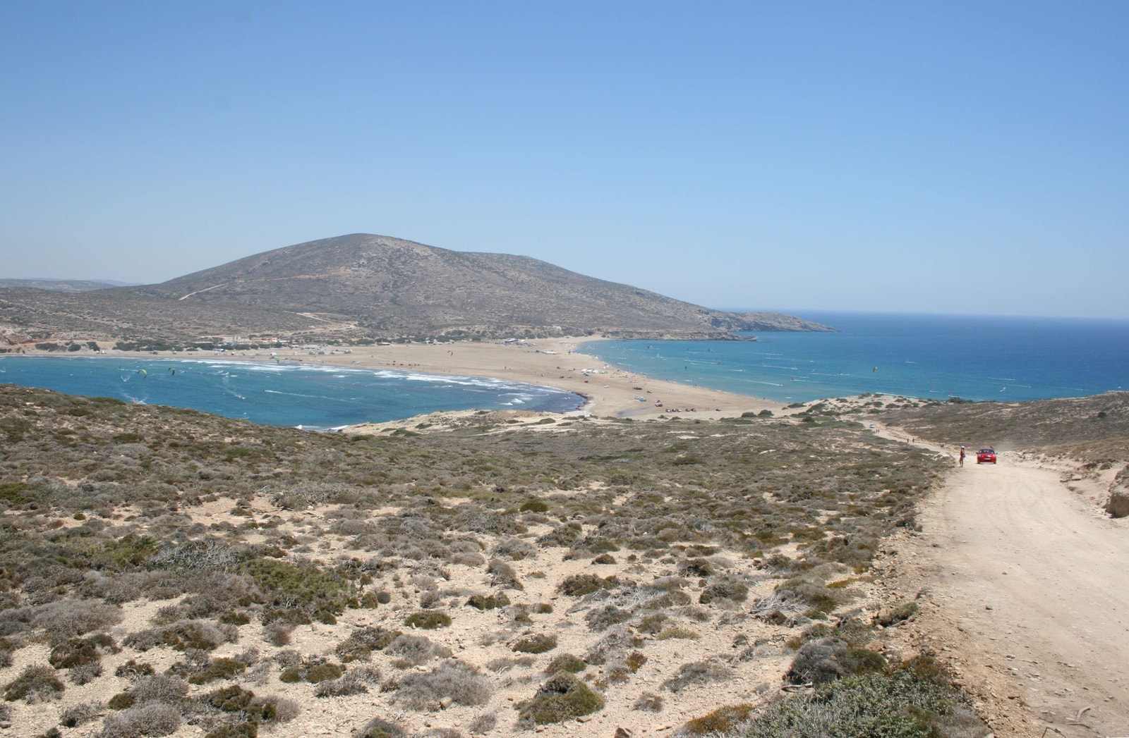 A long, narrow sandbar separates two distinct bodies of blue water, connecting the main island to a smaller, rocky one.