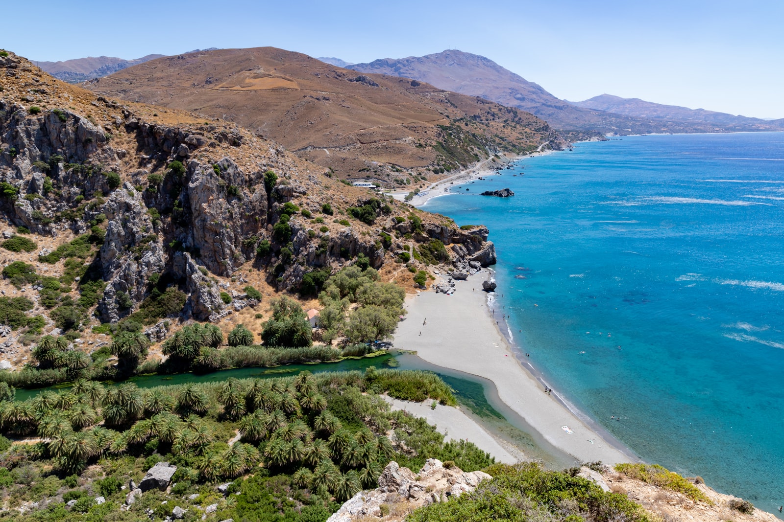Aerial view of a palm-filled river valley winding towards a sandy beach