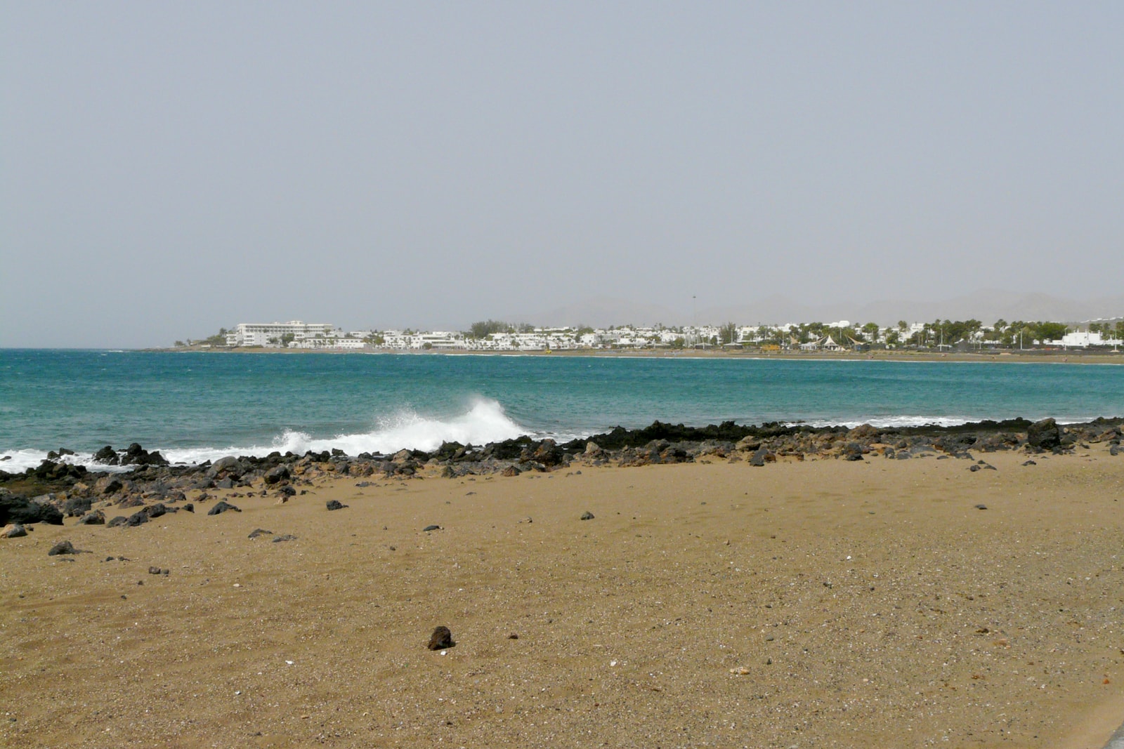 A long sandy beach curves towards the resort town of Puerto del Carmen in the distance.