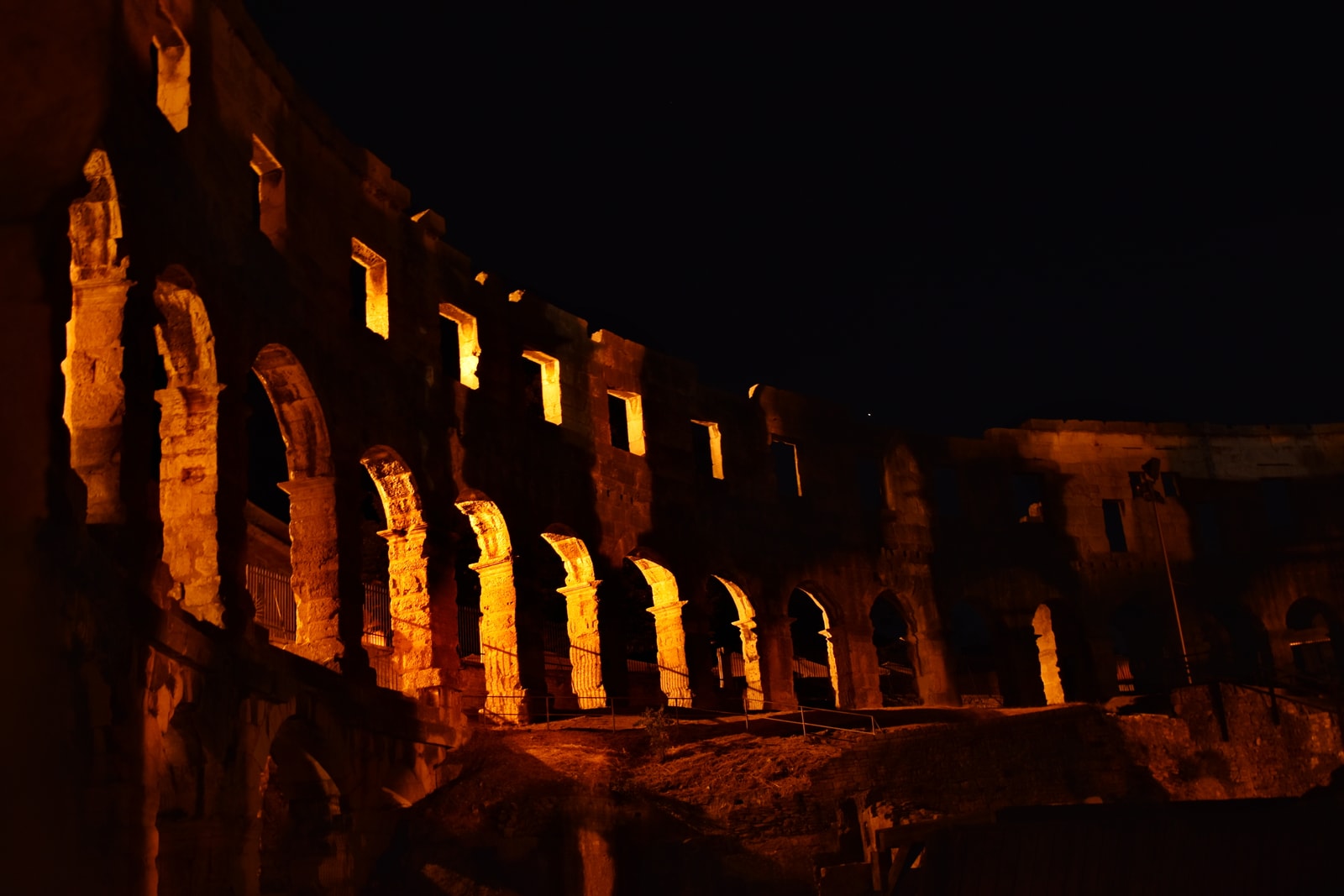 The Pula Arena illuminated with warm golden light at night, creating a dramatic venue for summer concerts and events.