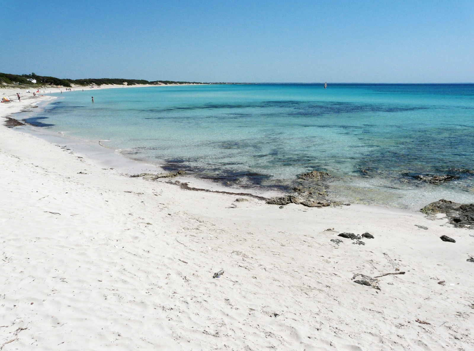 A view of the pristine, calm, and shallow crystalline turquoise water at Punta Prosciutto, with white sand in the foreground.