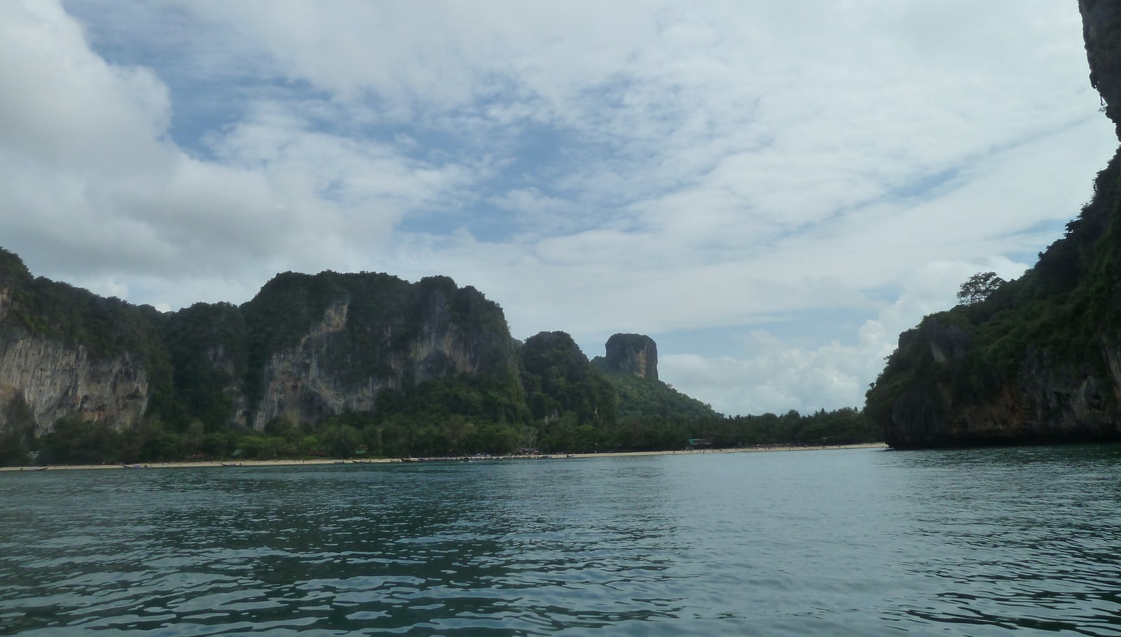 Several limestone karst towers rise dramatically from the rippling turquoise sea under a slightly hazy sky.