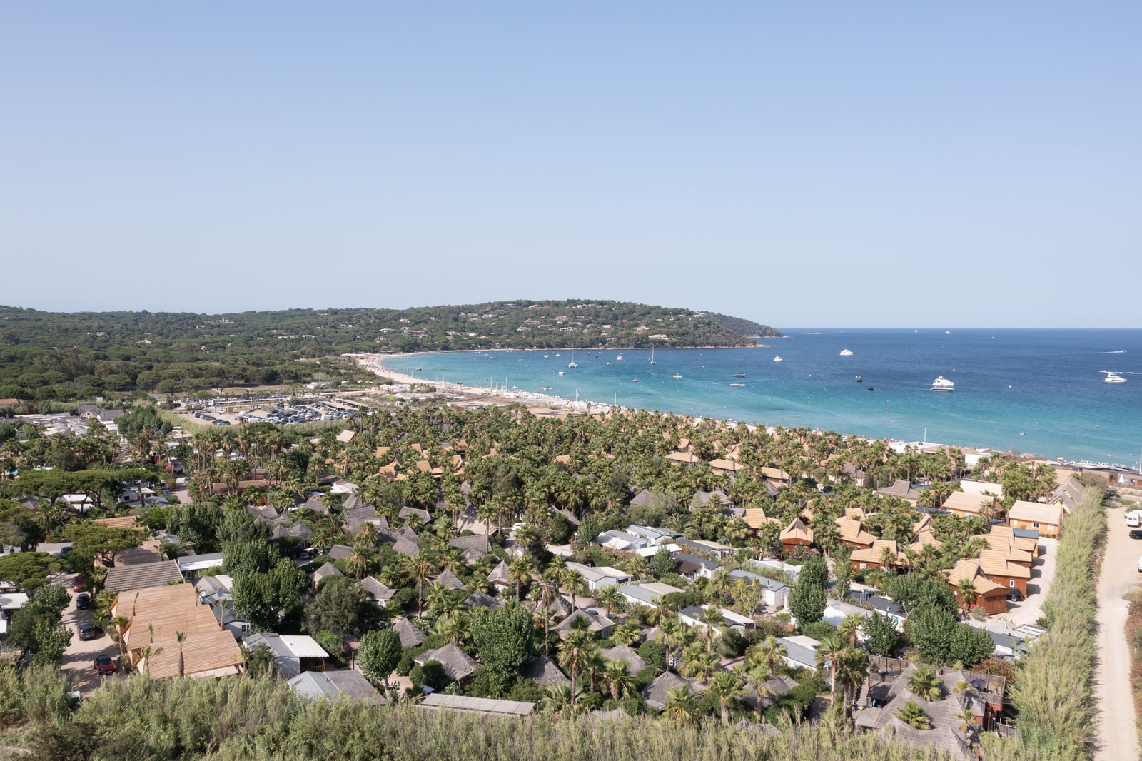 Aerial view of resort bungalows nestled within a canopy of palm trees right next to the sea.