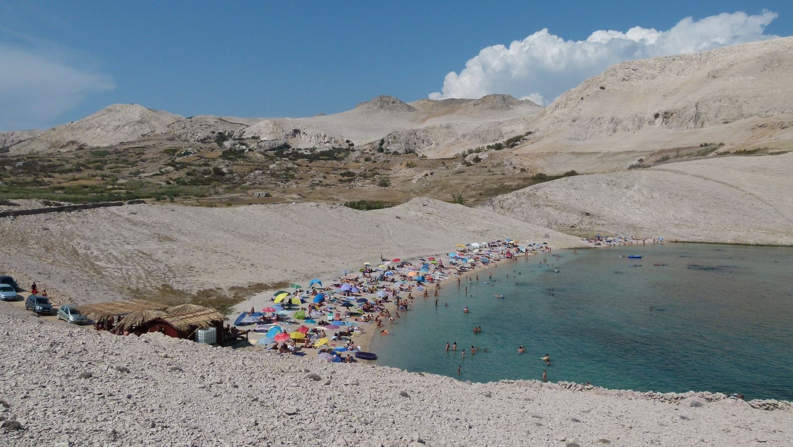 A panoramic view of Ručica Beach's crescent bay surrounded by barren, moon-like hills.