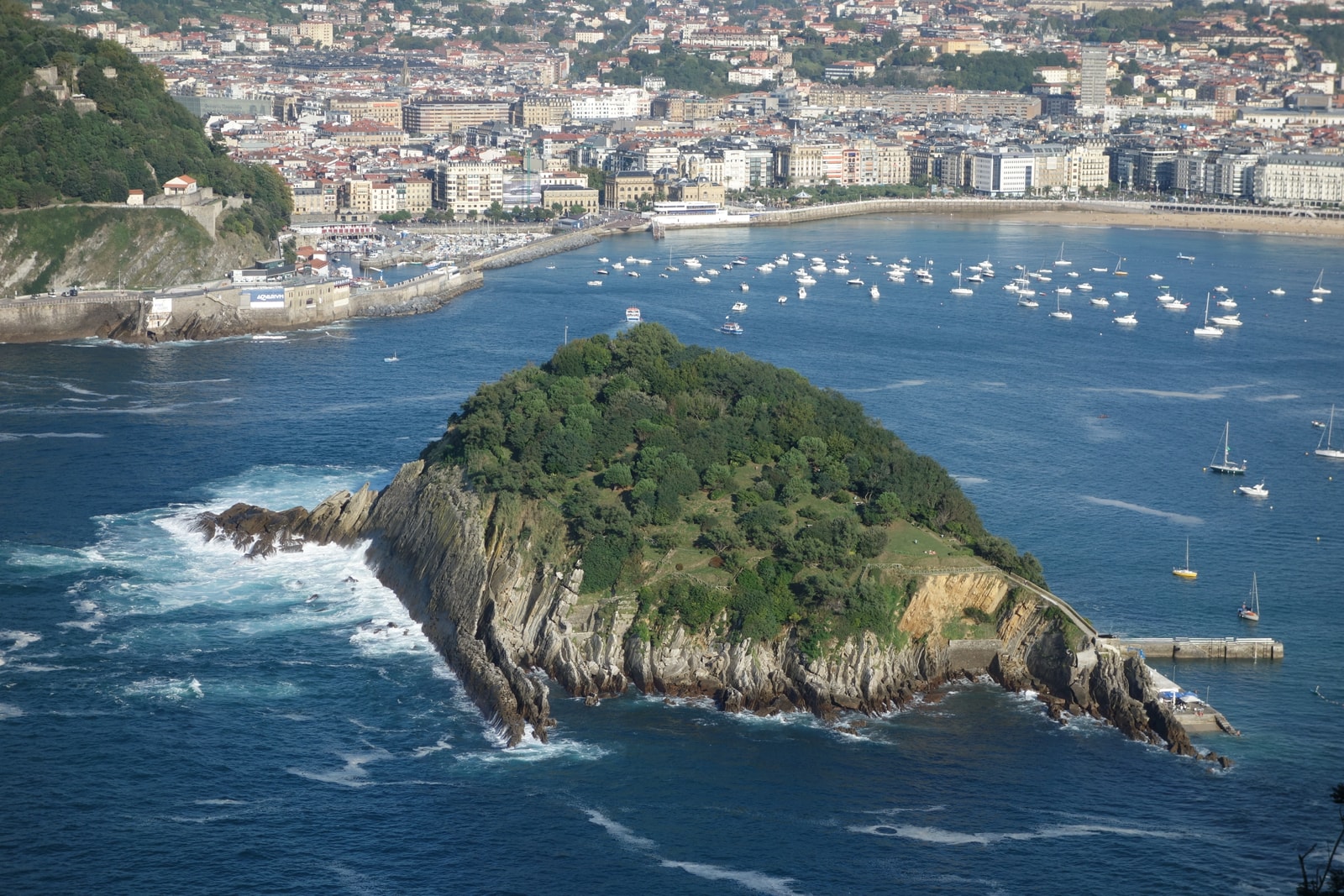 A view of Santa Clara Island's rugged cliffs and lush green top, with sailboats in the blue water of La Concha Bay.