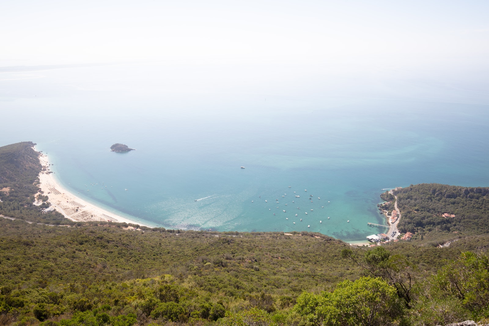 High-angle panoramic view of the turquoise water and sandy shoreline of Portinho da Arrábida in Setubal