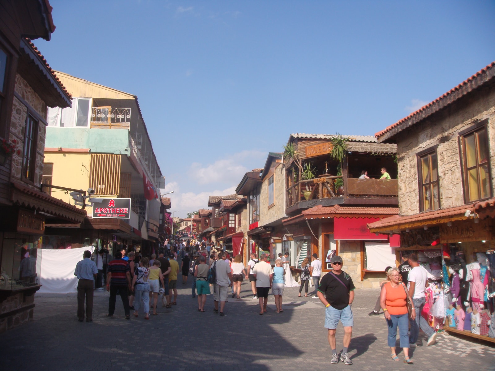 A busy commercial street in Side is lined with shops and restaurants under colorful awnings.