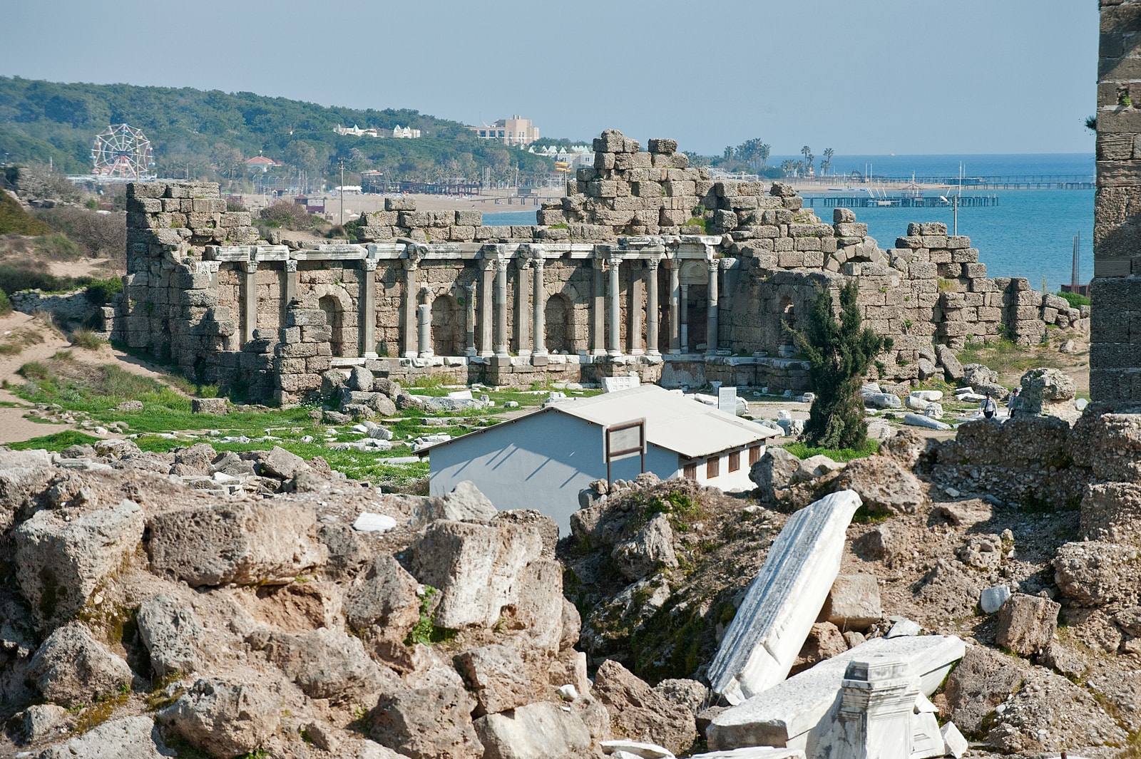 An elevated view of the State Agora ruins in Side, with the modern town and the Mediterranean Sea in the background.