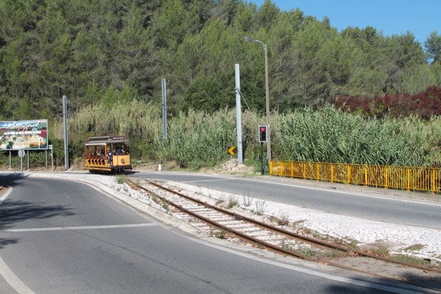 The historic open-sided wooden carriage of the vintage 1904 Sintra Tramway rolling through green countryside