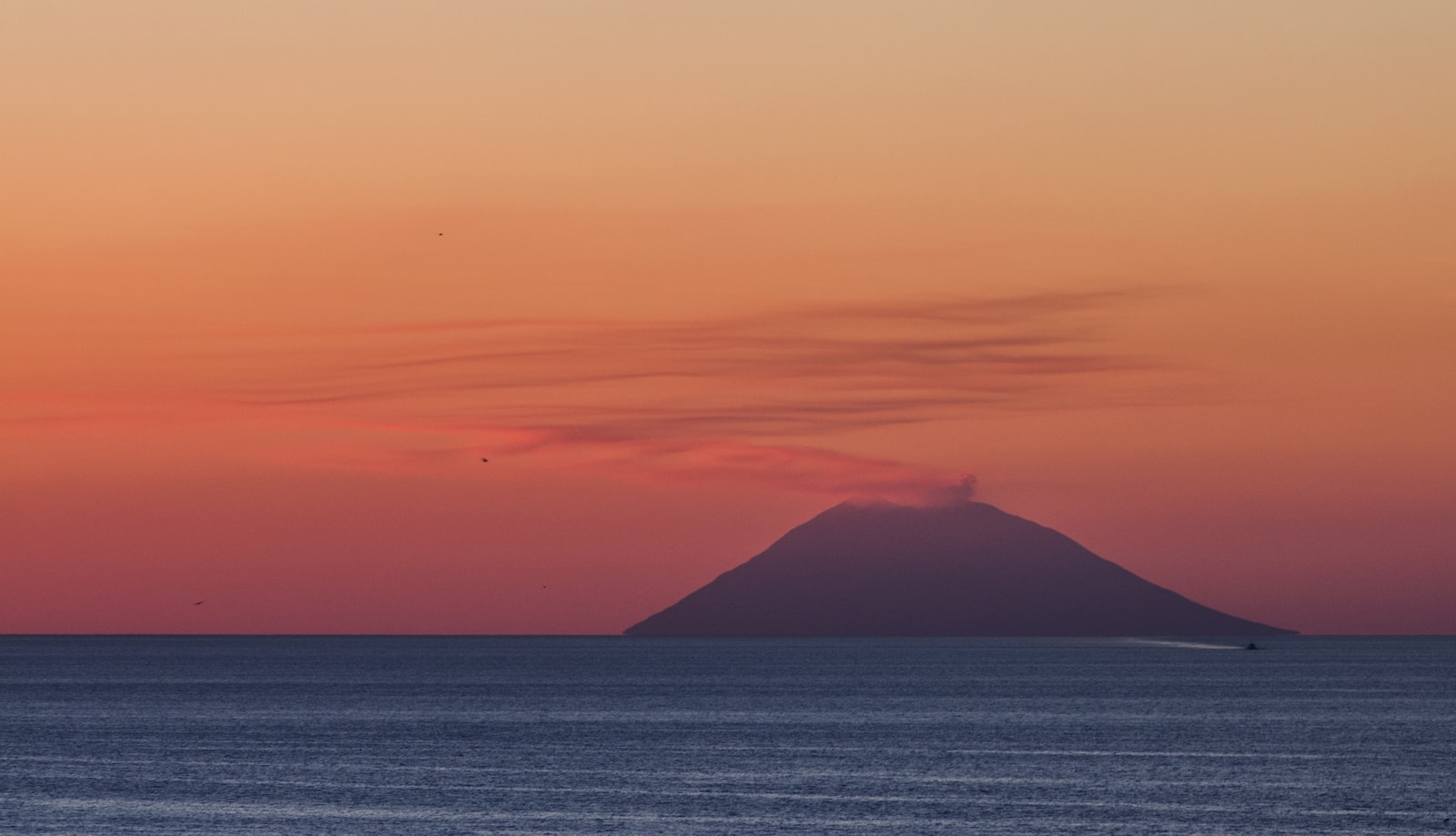 The active Stromboli volcano smoking on the horizon, silhouetted against a colorful twilight sky.